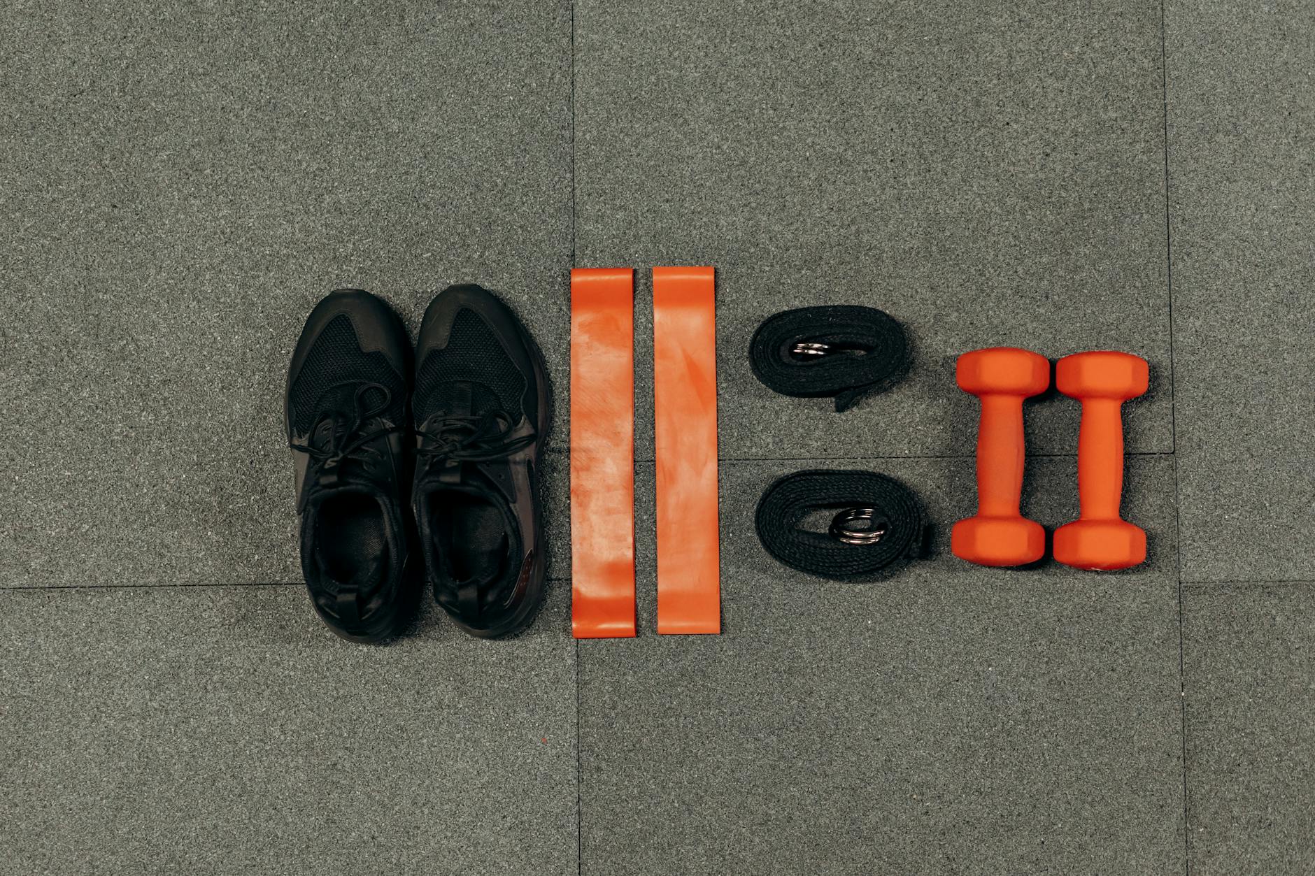Flat lay of gym essentials including dumbbells, sneakers, and resistance bands on a grey floor. - hiit workout for weight loss