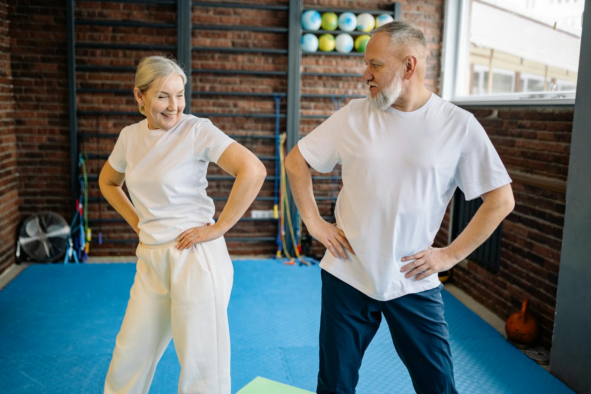 Elderly couple in white shirts having fun exercising indoors for fitness and wellness. - hip mobility exercises