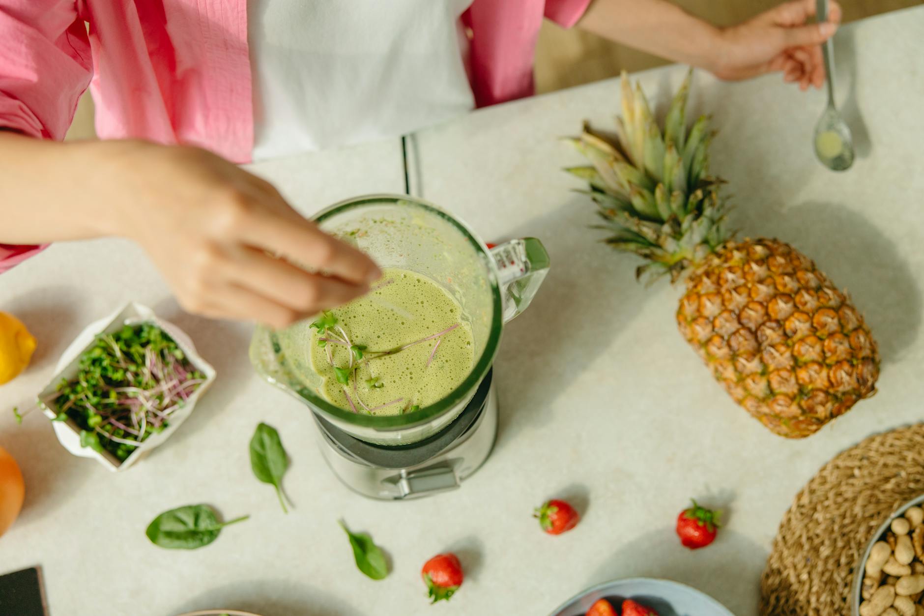 Top view of a green smoothie being prepared with pineapple and greens on a countertop. - kid-friendly smoothie recipes