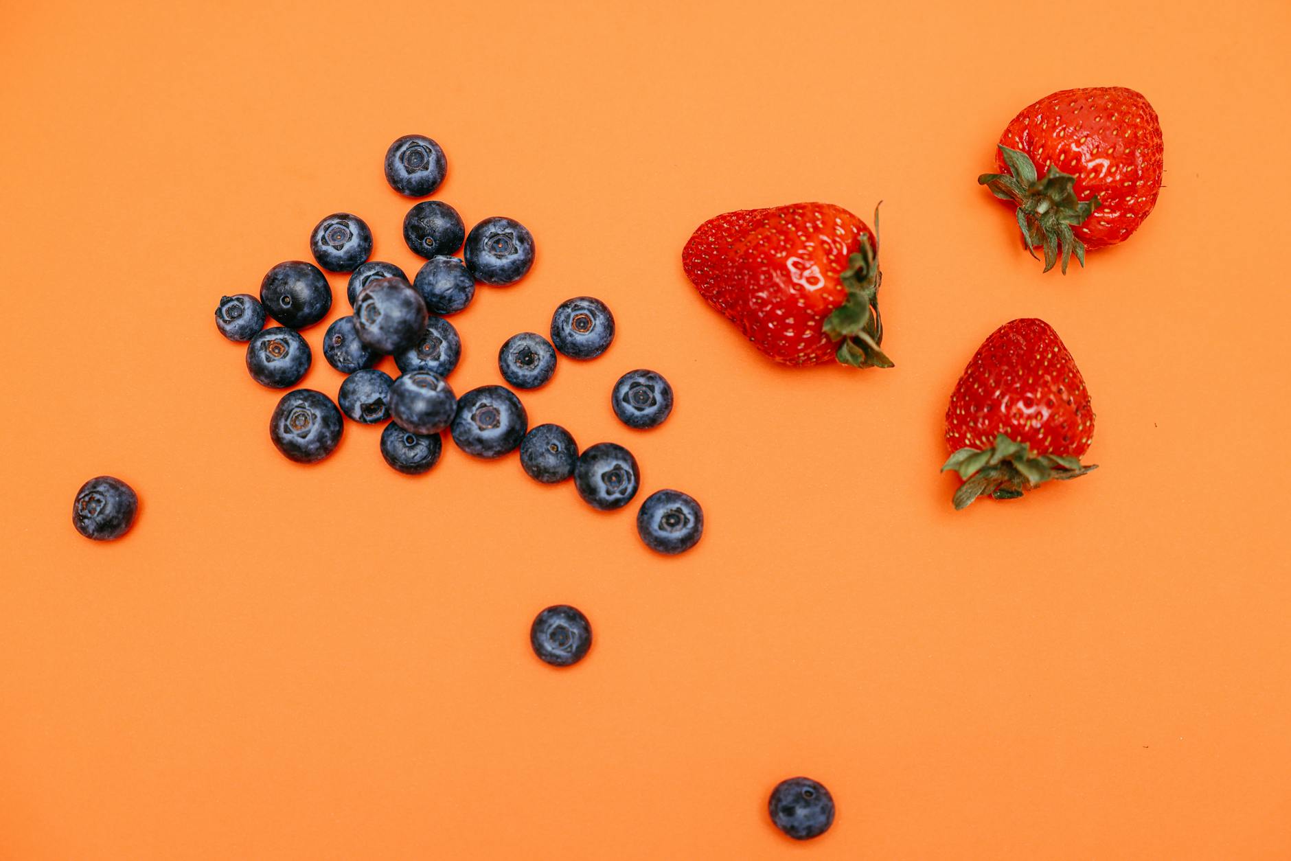 A vibrant still life of fresh blueberries and strawberries on an orange backdrop. - low calorie deficit