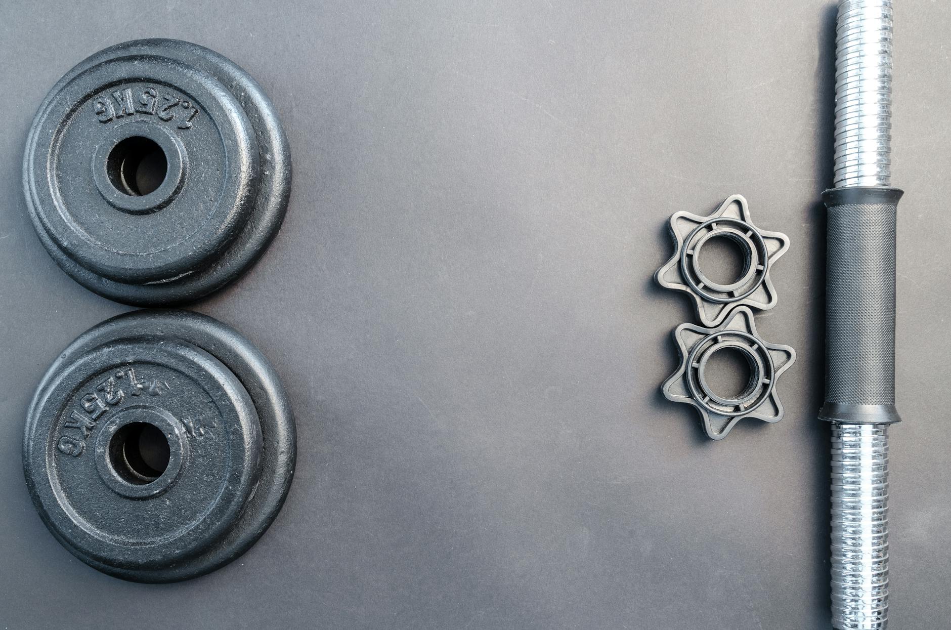 Barbell and two dumbbell weights arranged on a neutral gray surface. - mass building workout routine