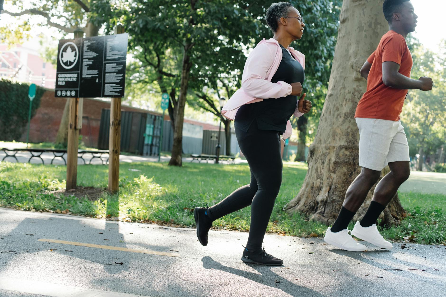 Two adults jogging on a sunny day in a green park, promoting fitness. - morning workout benefits