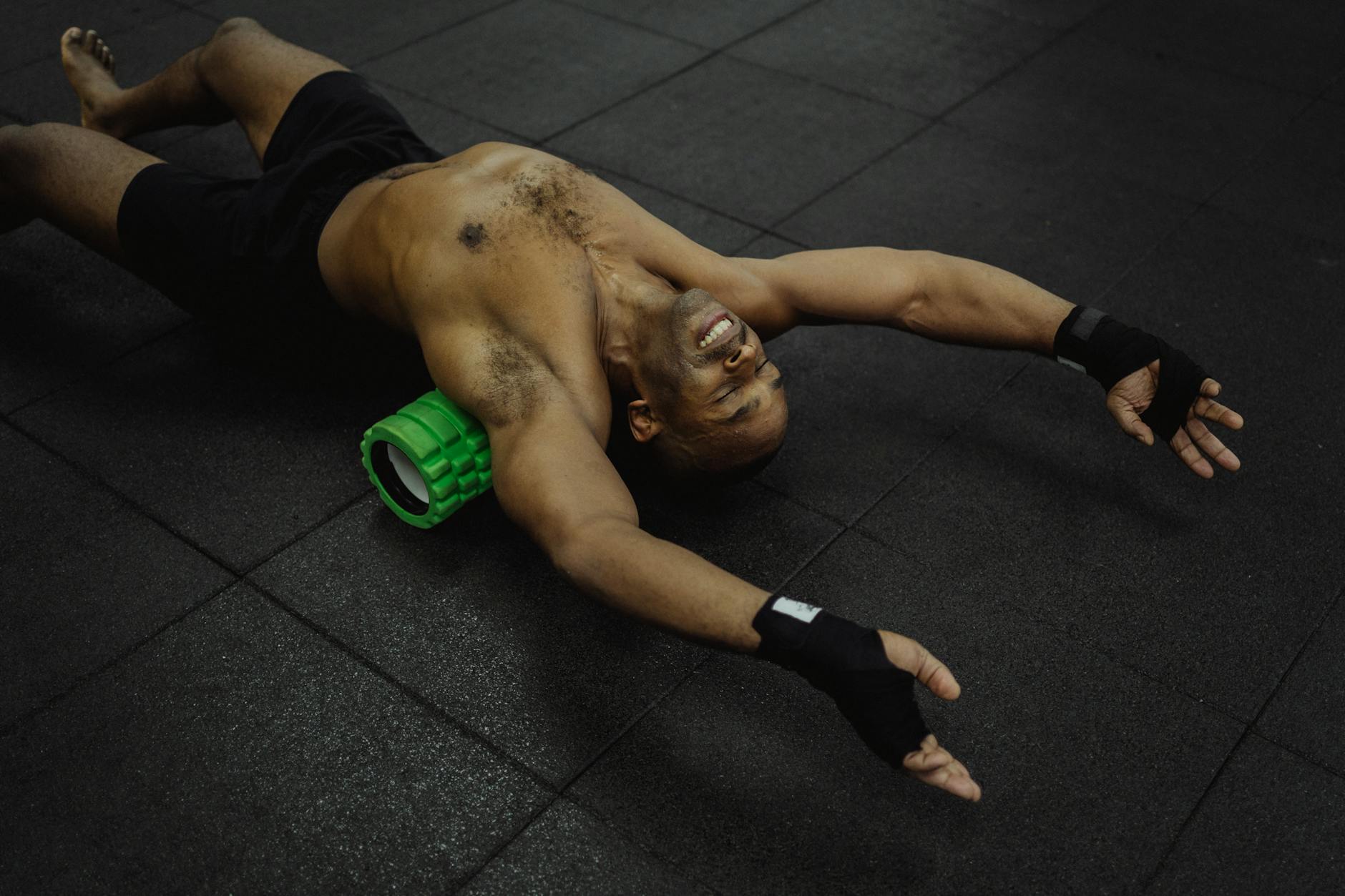 Shirtless man exercising with a foam roller in a fitness center. - muscle recovery after workout