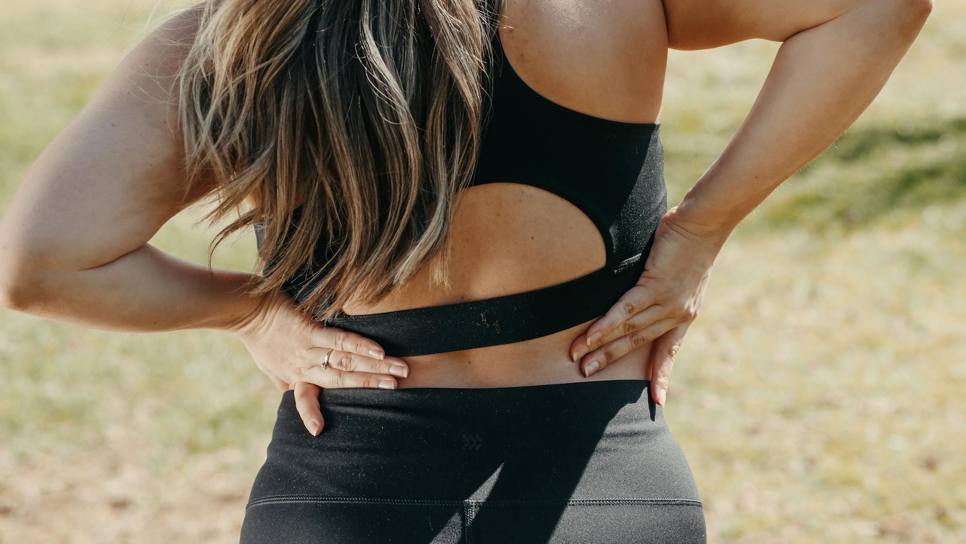 Close-up of a woman holding her back, suggesting back pain outdoors. - pilates for back pain
