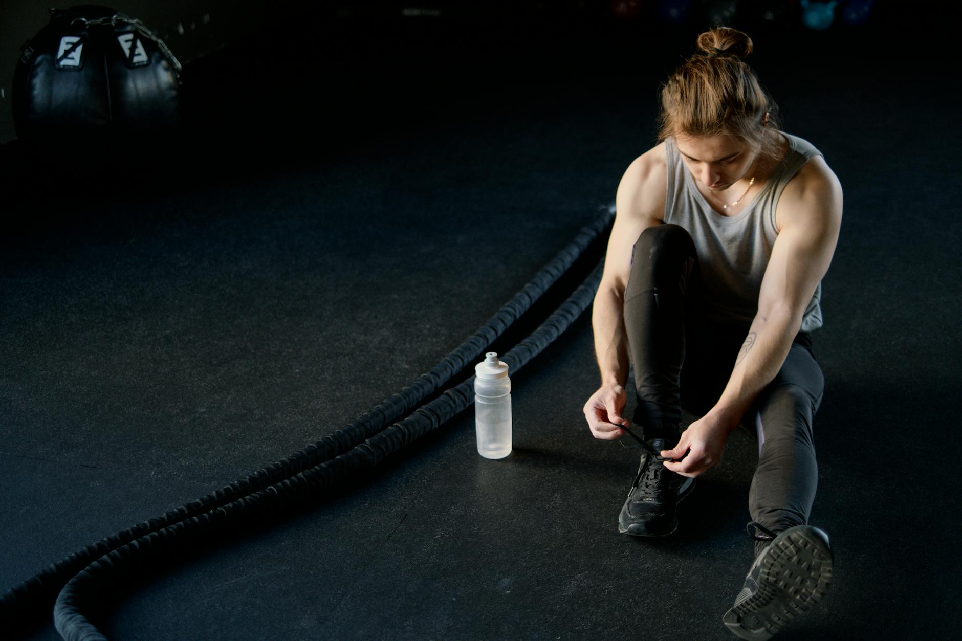 Man tying shoes on gym floor with battle ropes and water bottle, ready for training. - pre workout nutrition guide