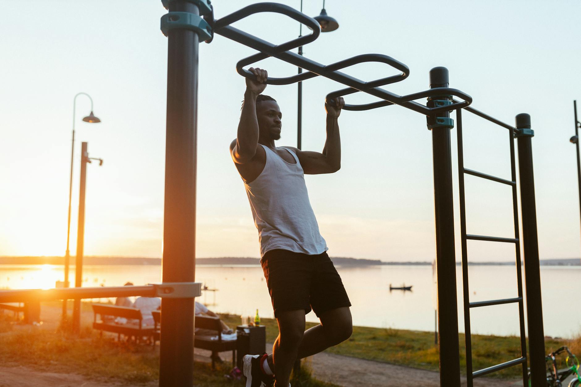 Man performing pull-ups on outdoor gym equipment by the lake during sunset. - push pull workout routine