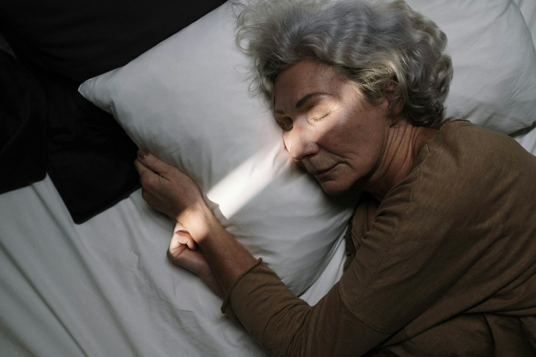 A serene moment of an elderly woman peacefully sleeping on a bed with soft lighting. - what is sleep hygiene