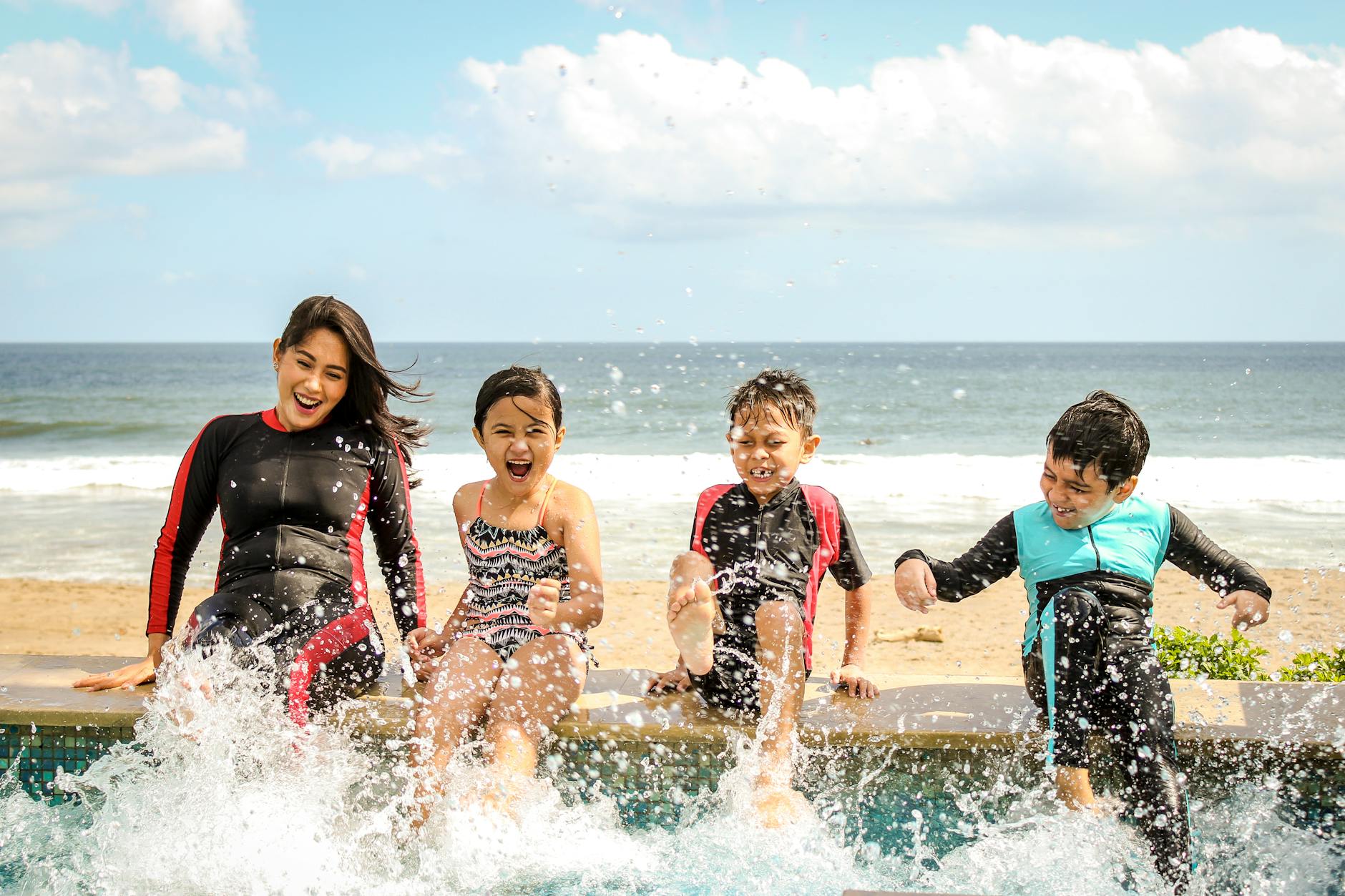 A family having fun splashing water near the seashore on a sunny day in Bali, Indonesia. - swimming benefits for children