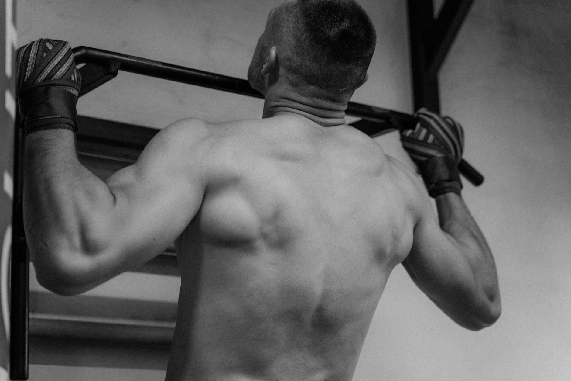 Back view of a shirtless man doing pull-ups, showcasing strength and fitness. - upper back posture exercises