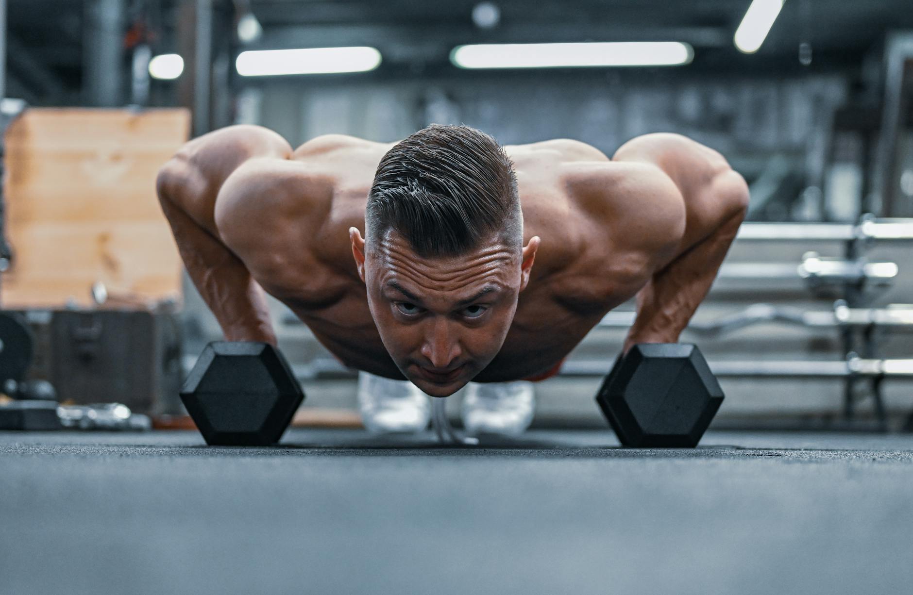 Fit man doing push-ups on hex dumbbells in a modern gym setting. - upper body cardio workout