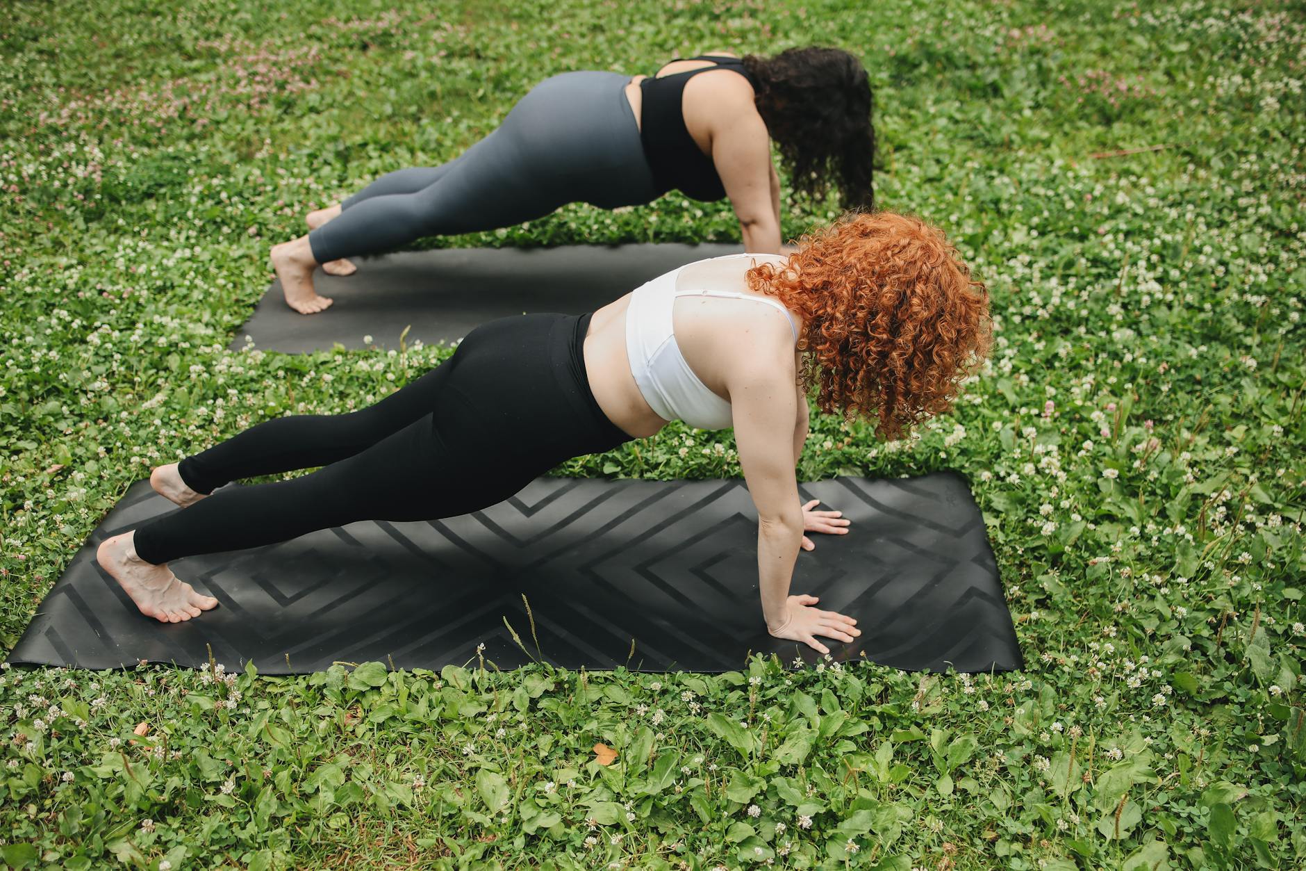 Two women holding a plank position on yoga mats outdoors in a lush green setting. - abs workout