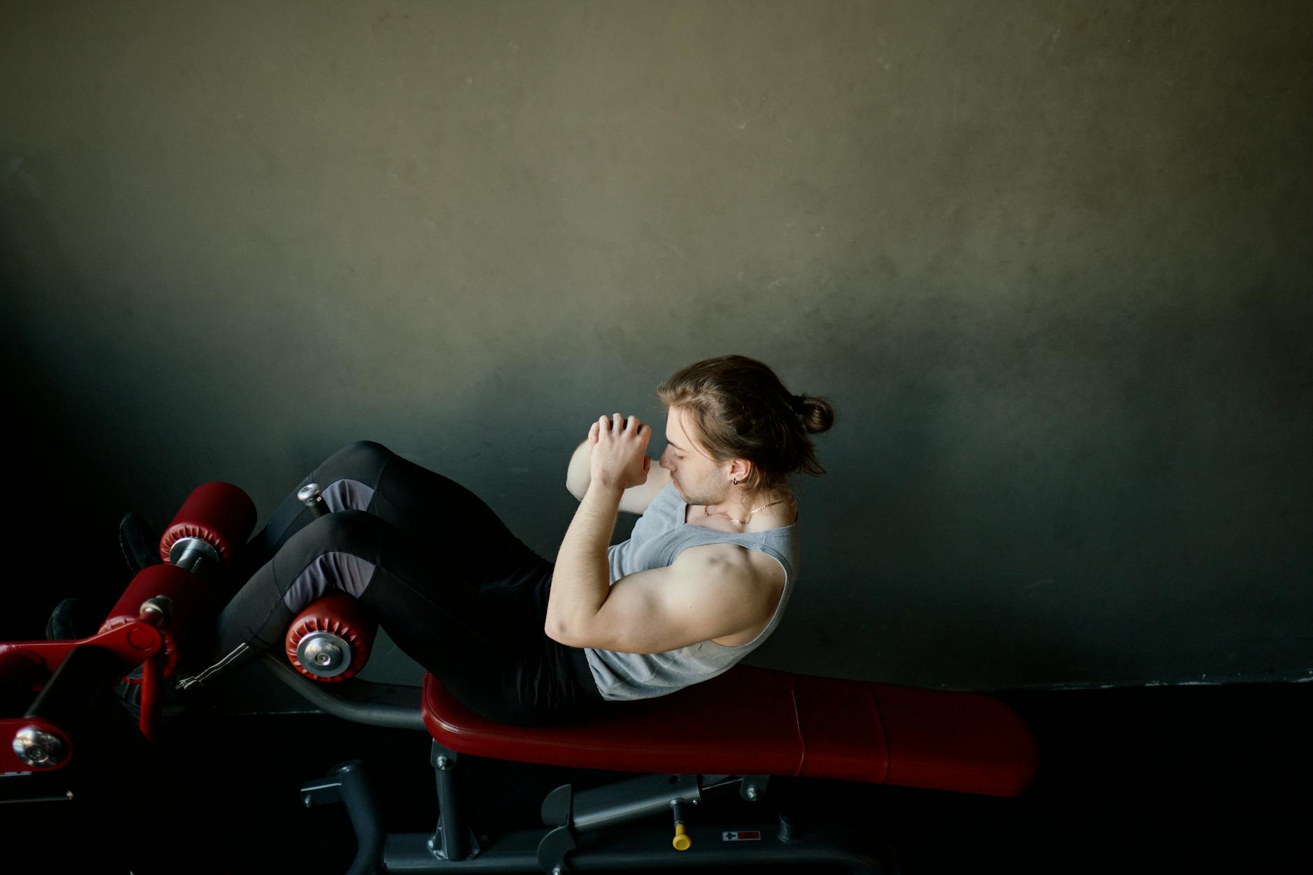 Focused young man doing abdominal exercises on a gym bench. - abs workout