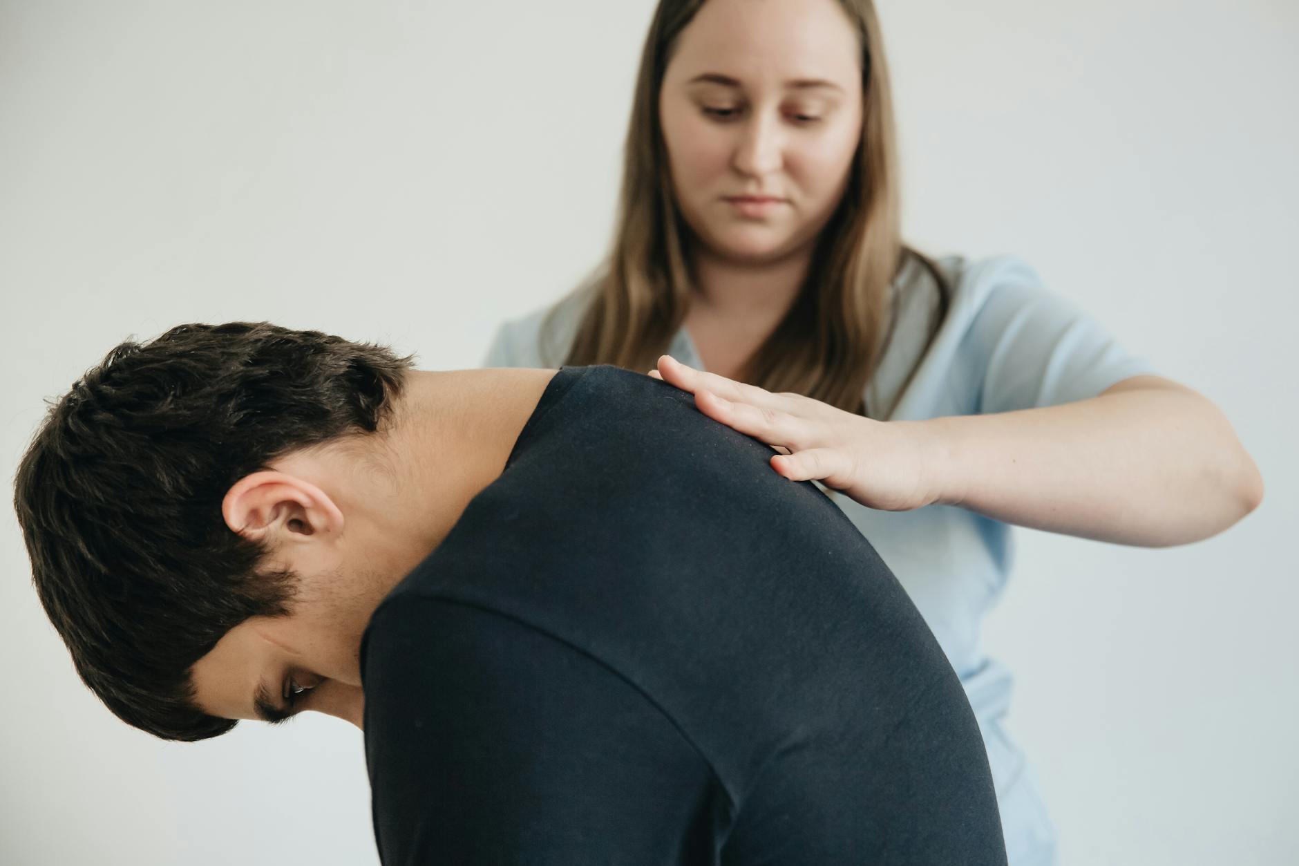 A physiotherapist assisting a patient with back pain in an indoor clinic setting. - arthritis back pain