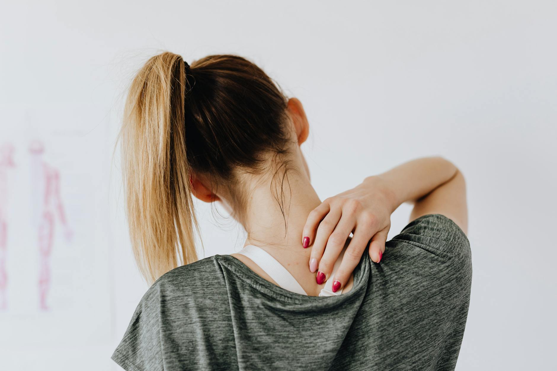 A woman in casual clothing holds her neck, indicating pain or discomfort. - bad posture correction