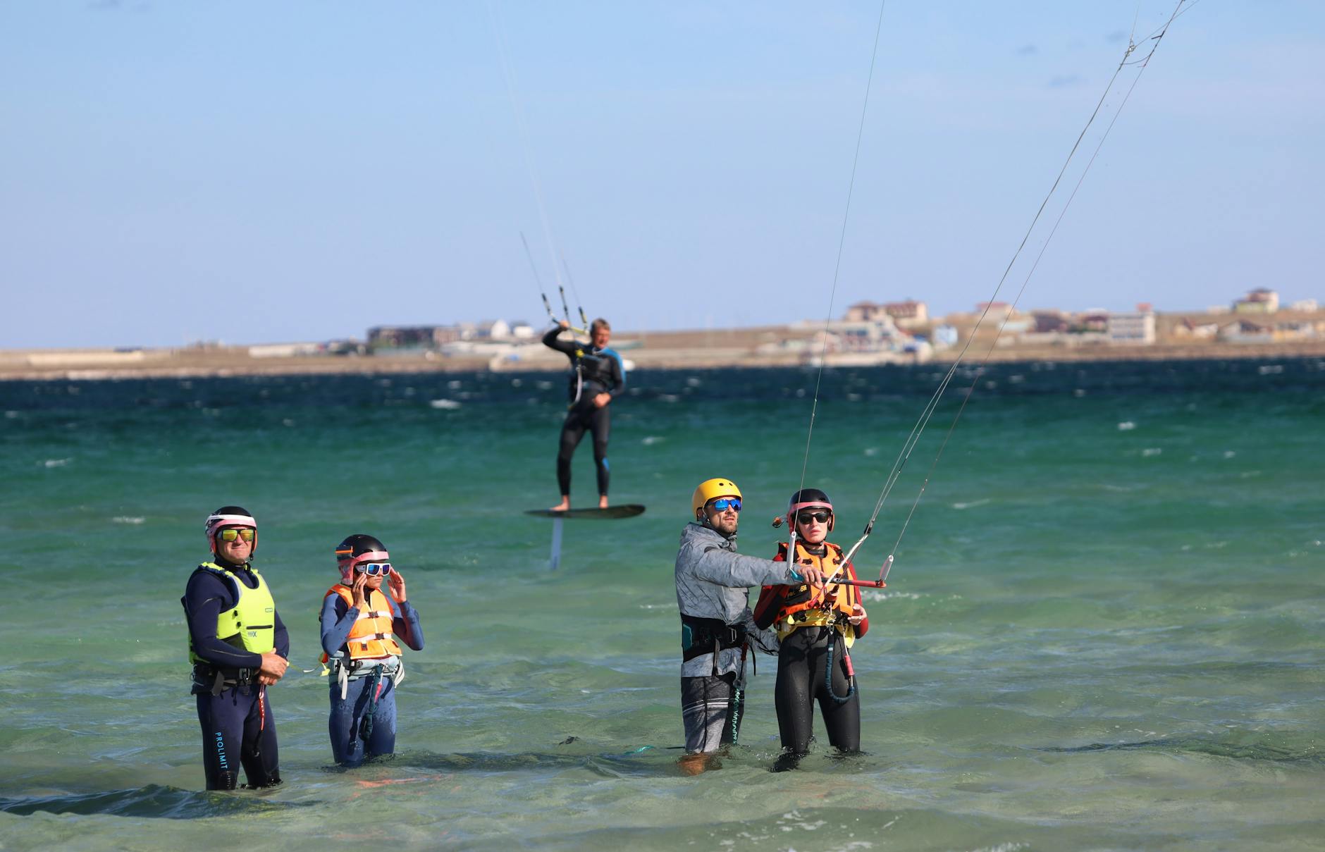 Instructors teaching kitesurfing in shallow sea waters with clear skies, offering a perfect leisure activity. - beginner exercises