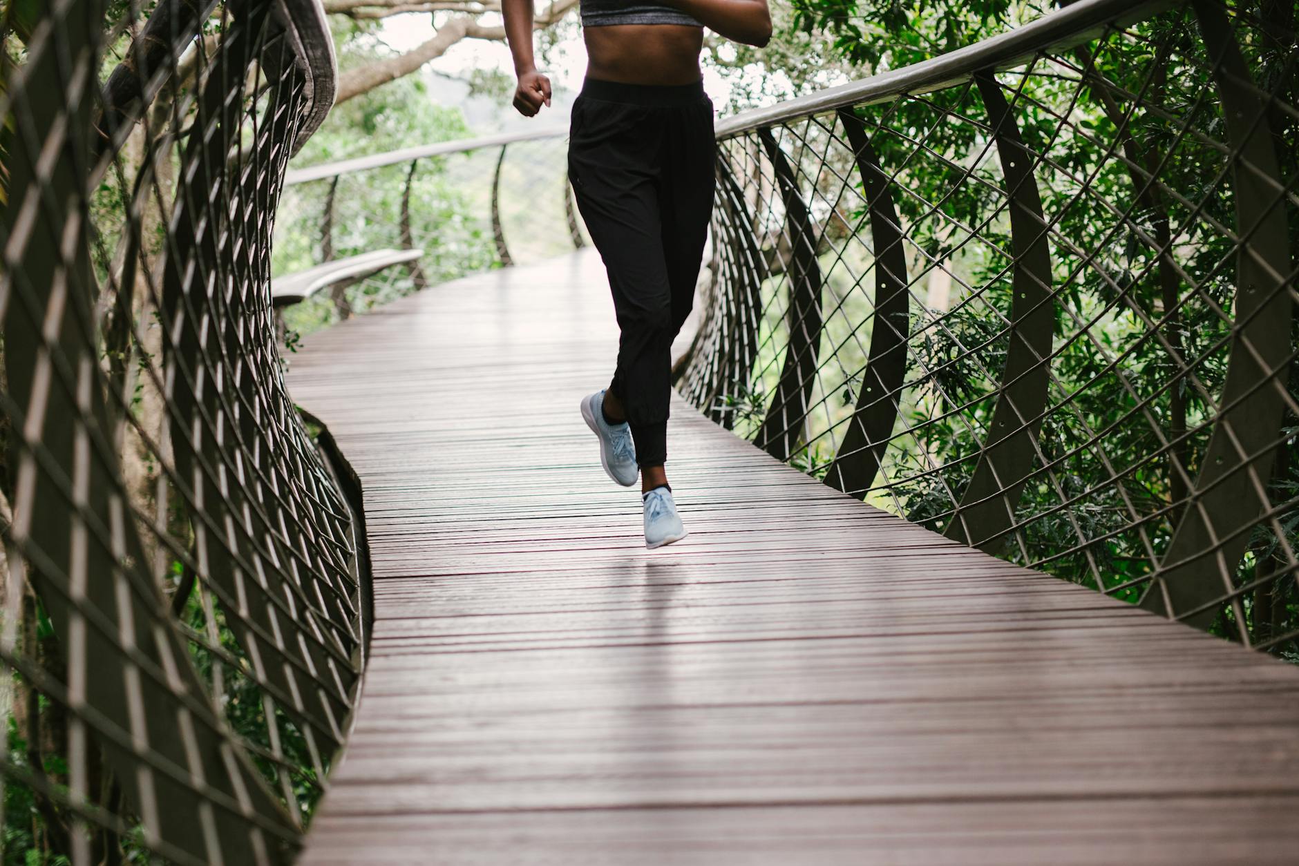 An athletic woman jogging on a nature trail bridge surrounded by greenery. - beginner running schedule