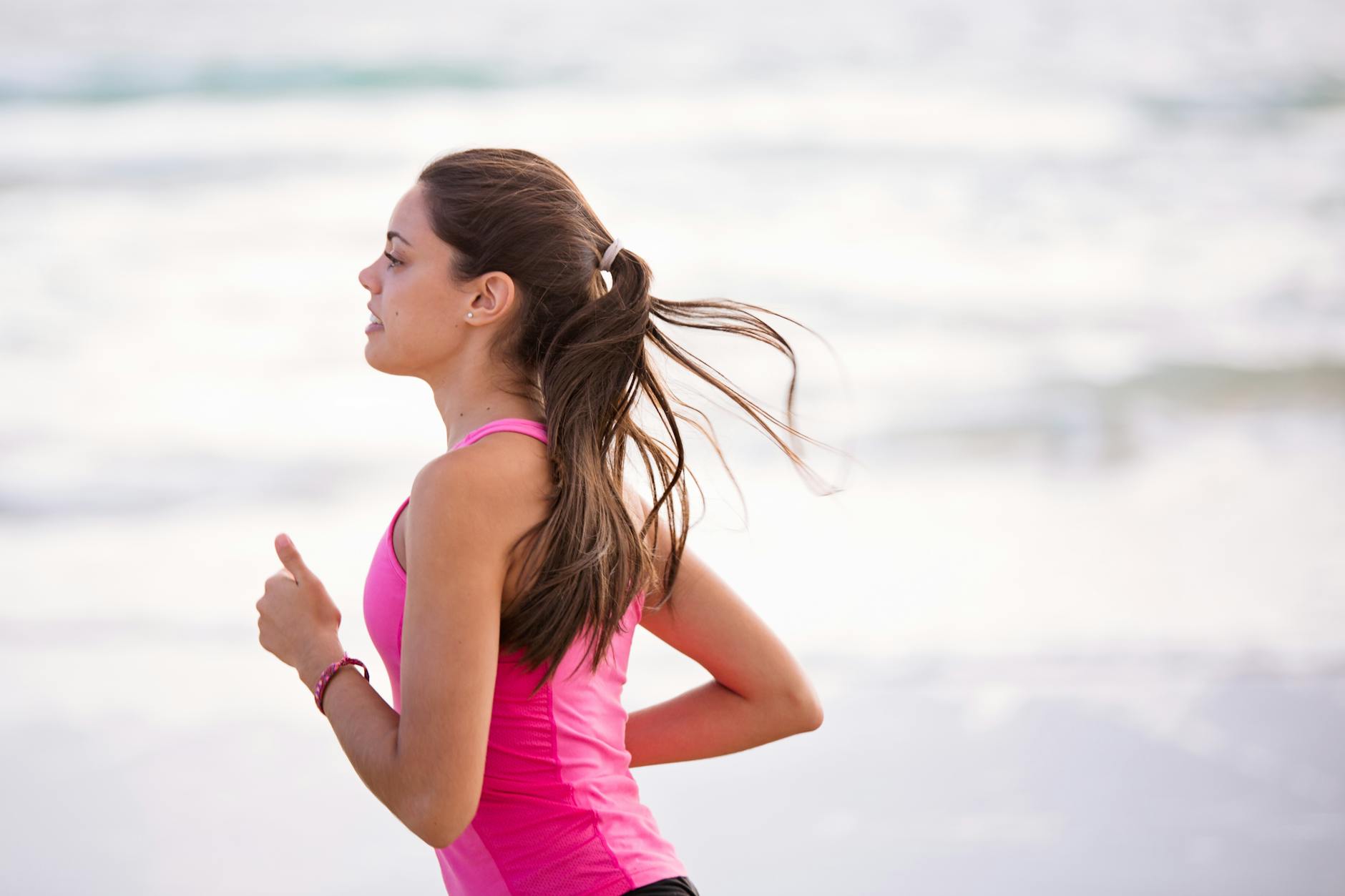 Side view of a young woman jogging on a beach wearing pink active wear. - beginner running tips
