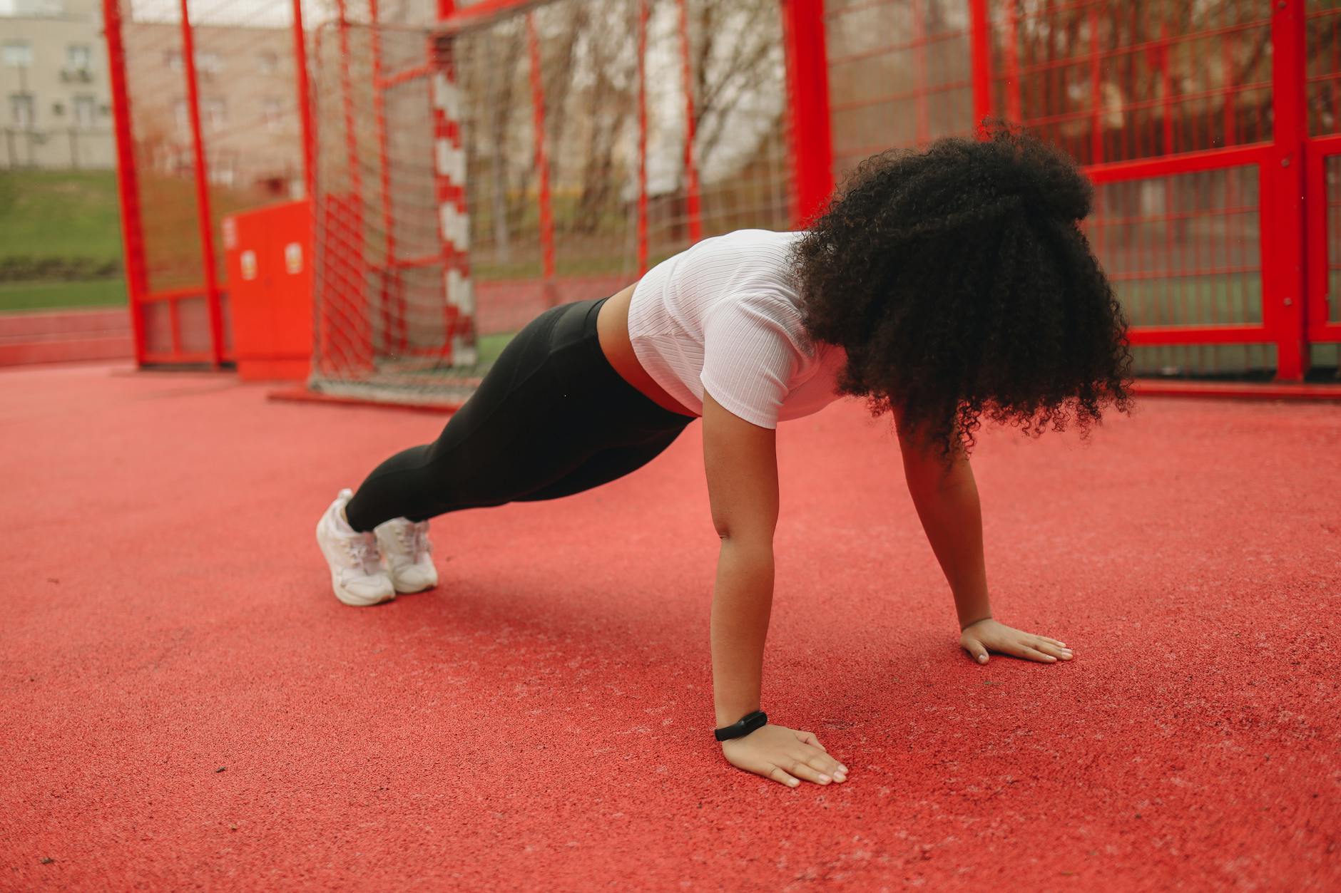 African American woman doing planks outdoors on a red sports track. Promoting a healthy lifestyle. - beginner workout routines