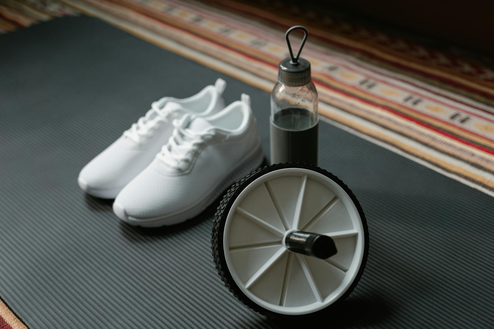 A close-up of white sneakers, ab roller, and water bottle on a yoga mat, ideal for fitness routines. - best ab workout