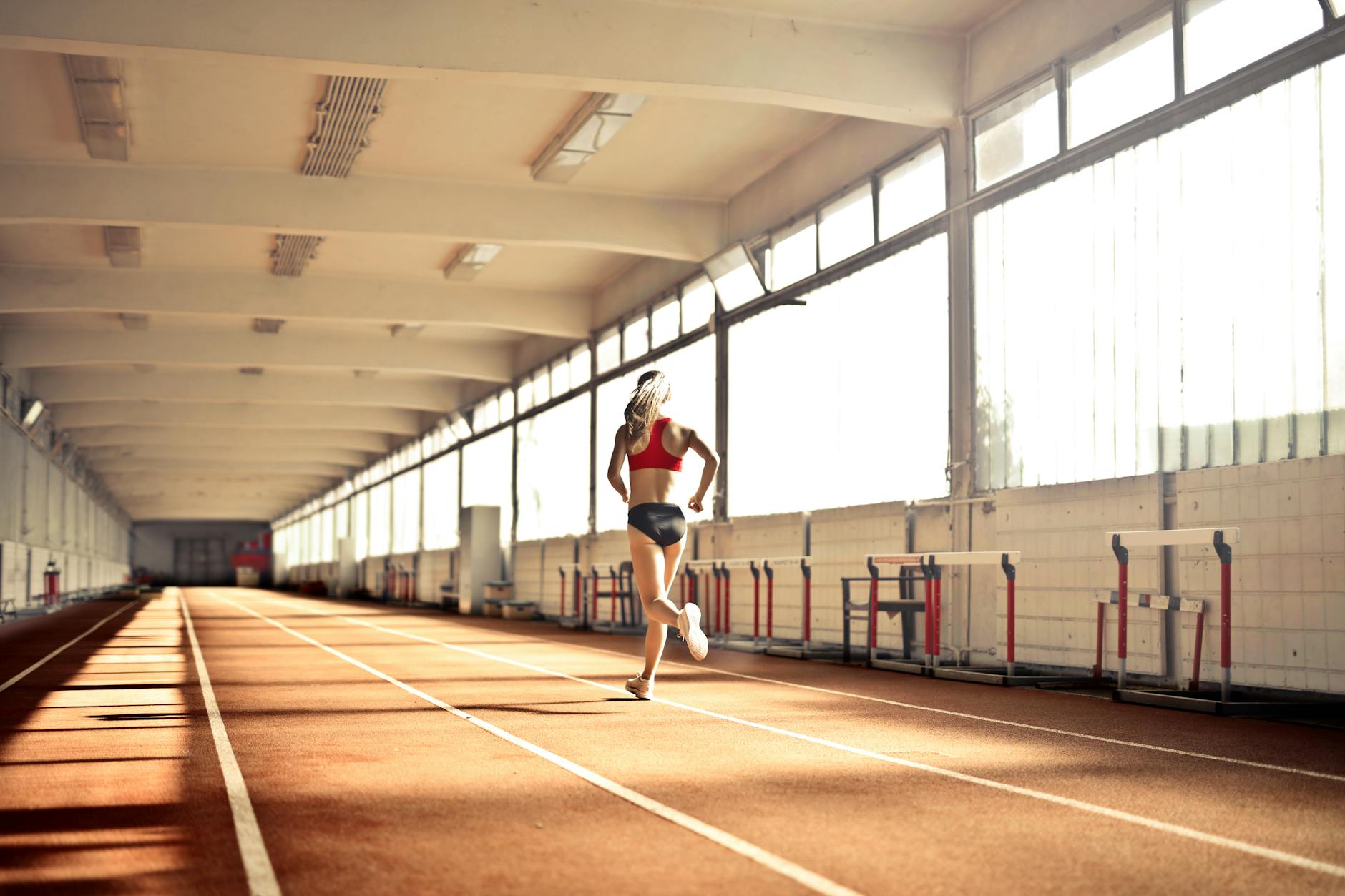 Woman in athletic wear running on an indoor track, showcasing speed and determination. - best back exercises