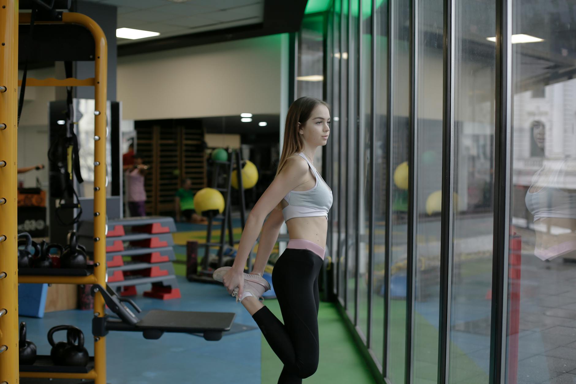 A young woman stretching inside a modern gym with large windows, focused on fitness. - best stretching routine