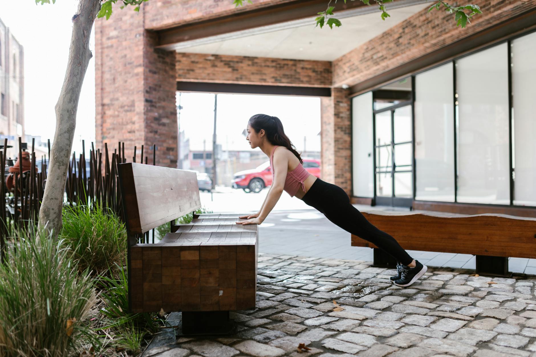 Asian woman performing calisthenics on a bench outdoors, showcasing a healthy lifestyle. - bodyweight shoulder exercises