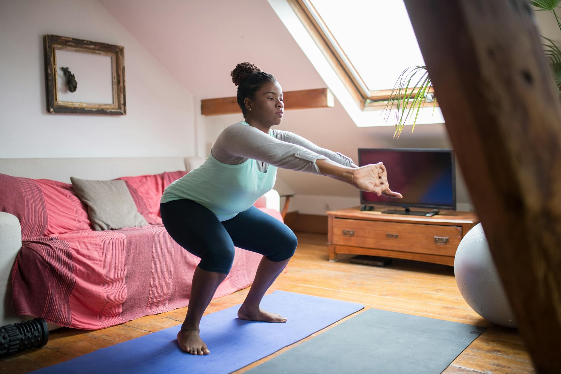A woman performs squats on a yoga mat in a cozy living room, promoting home fitness and wellness. - bodyweight workouts home