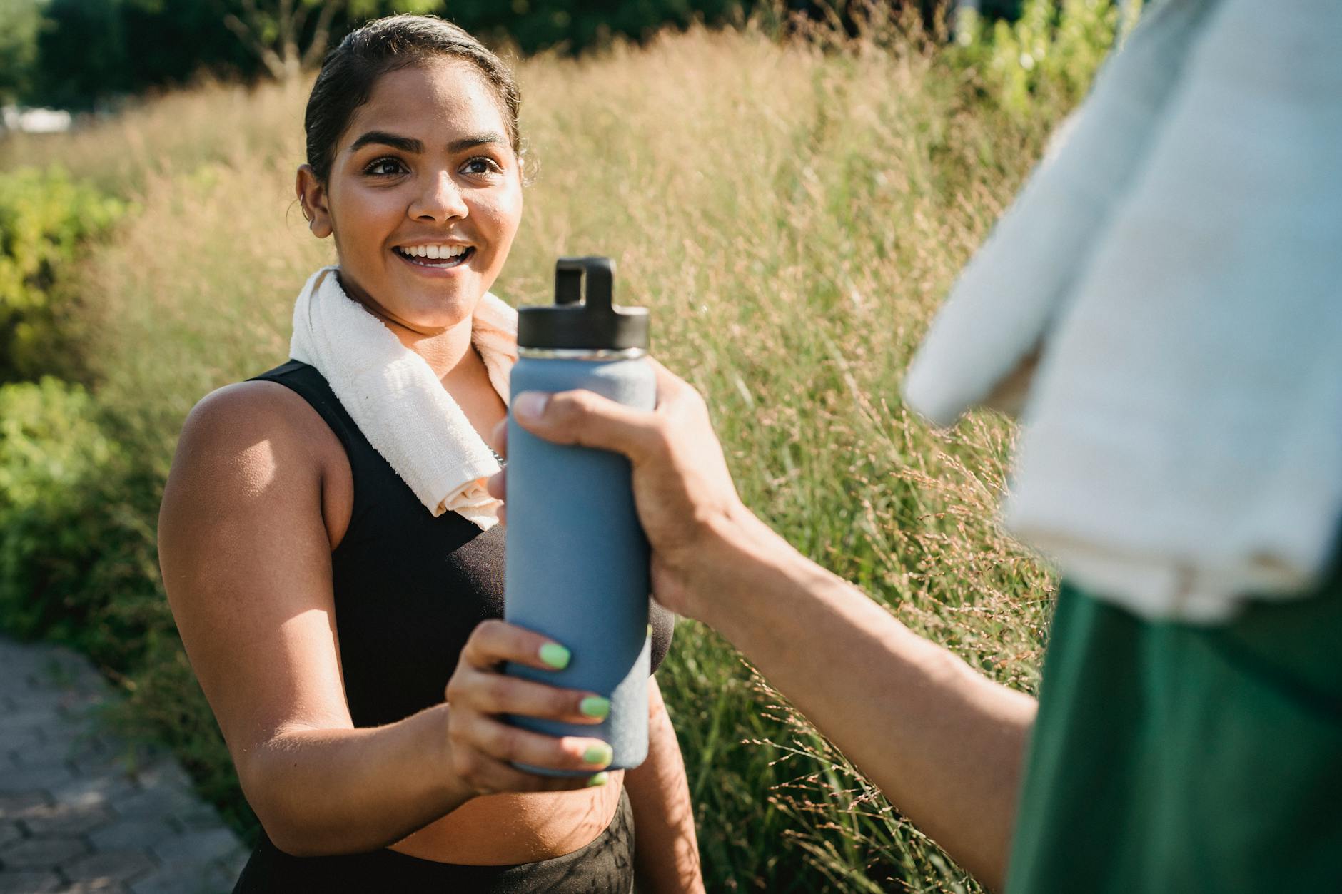 Smiling woman receiving water bottle during outdoor exercise. - boost energy naturally