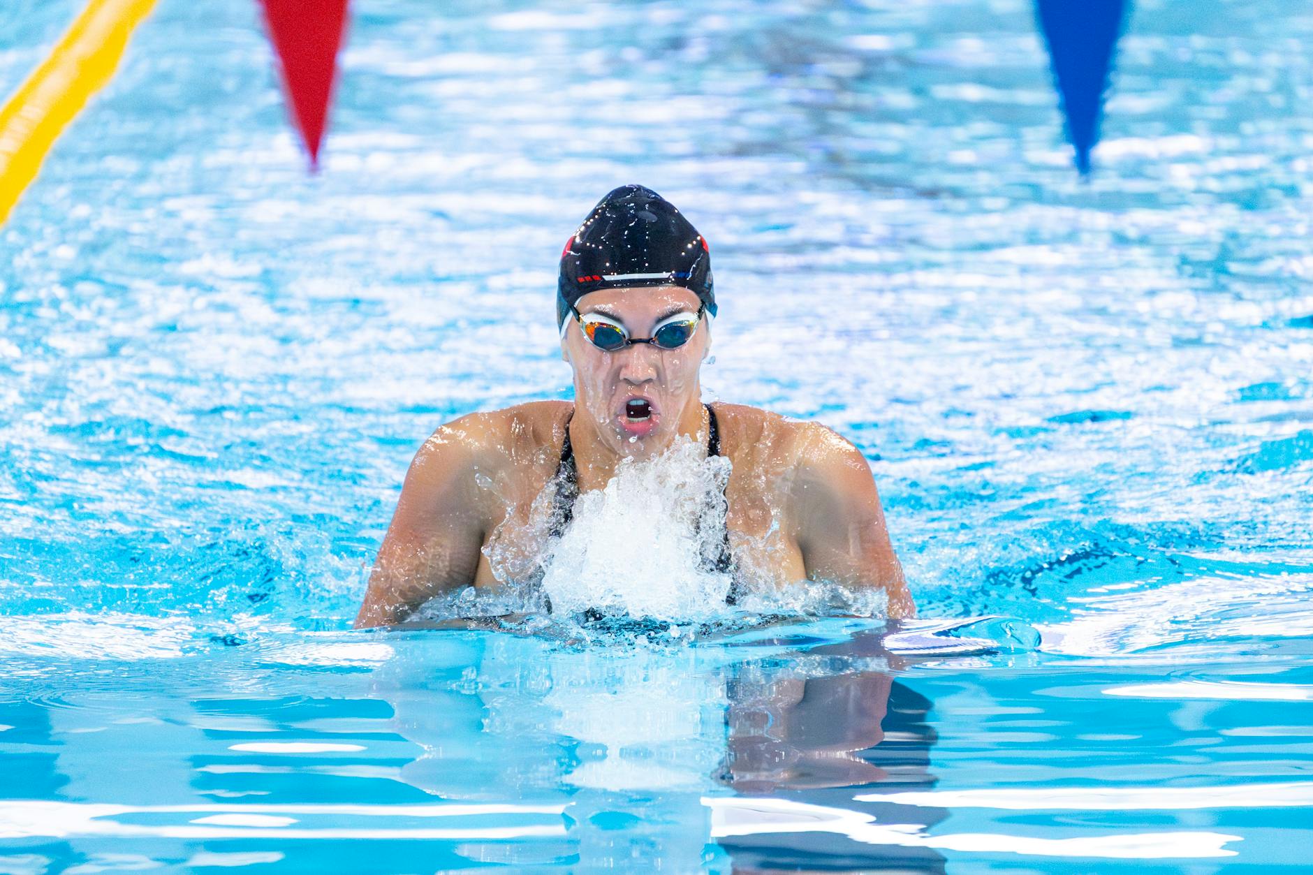 Professional swimmer in a race, captured mid-stroke with vibrant pool water. - breaststroke swimming benefits