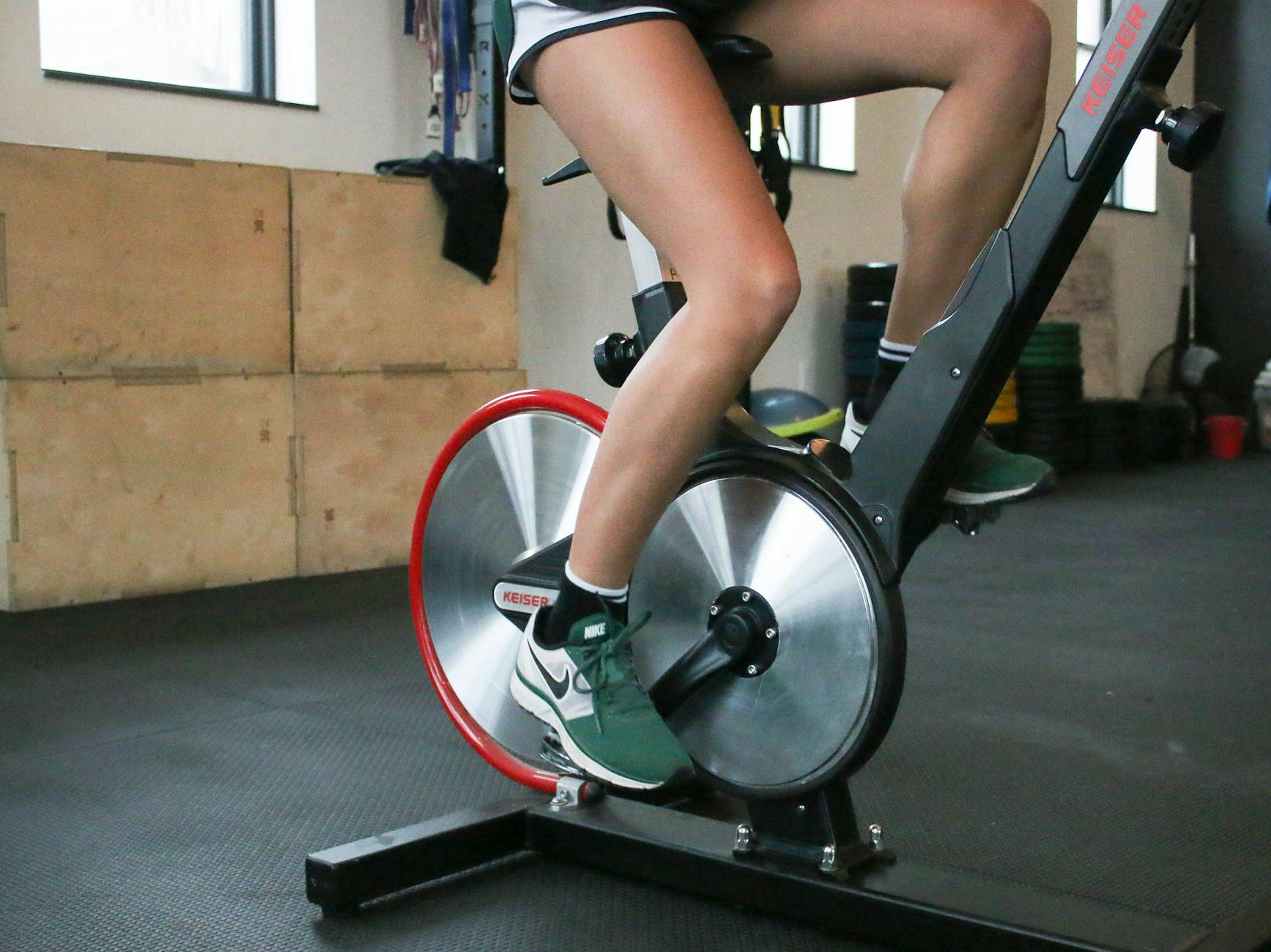 A woman cycling on a stationary bike indoors, focusing on fitness and leg muscle strength. - carb cycling workout