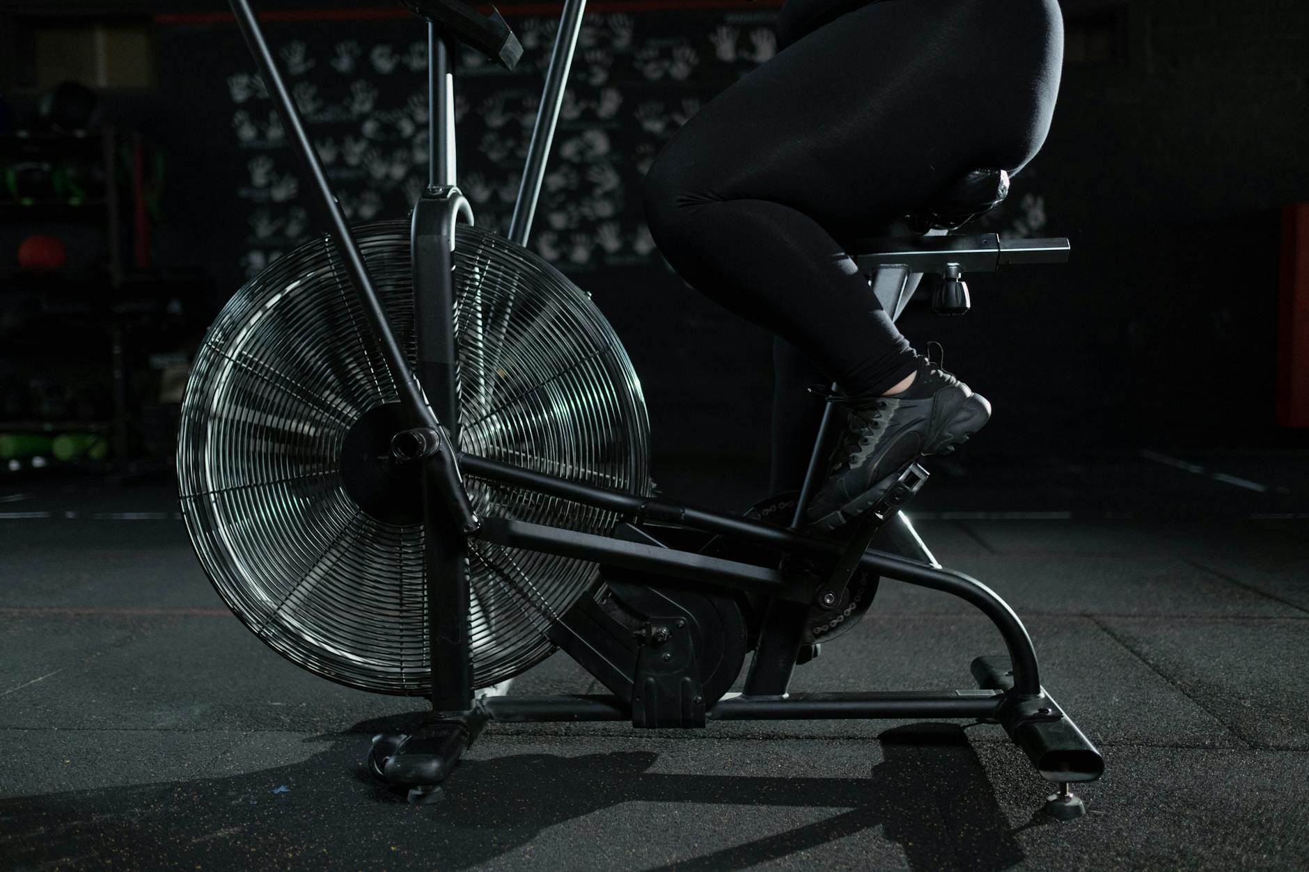 Close-up of a woman exercising on a stationary bike in a dimly lit gym. - carb cycling workout