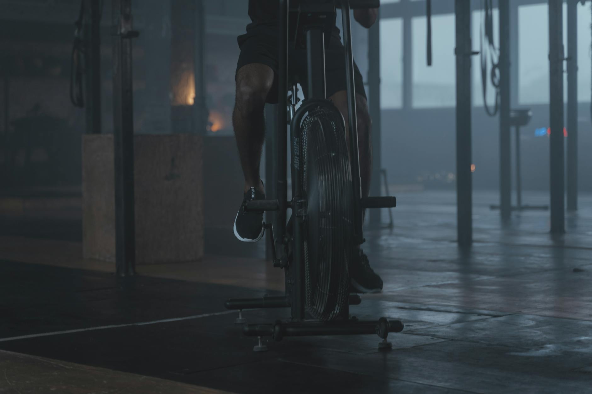 Close-up of a person exercising on a stationary bike in a dimly lit gym setting. - cardio fat burning