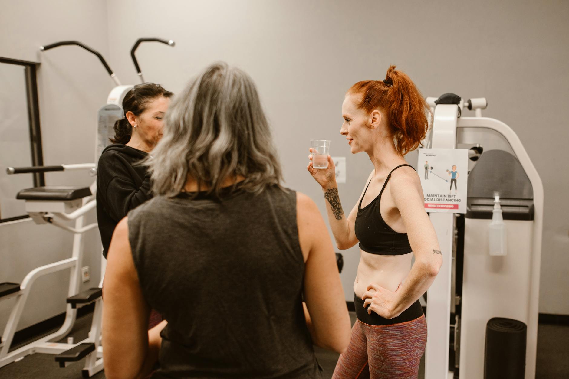 Three women chatting and hydrating in a gym environment, focusing on wellness and fitness. - cardio for women
