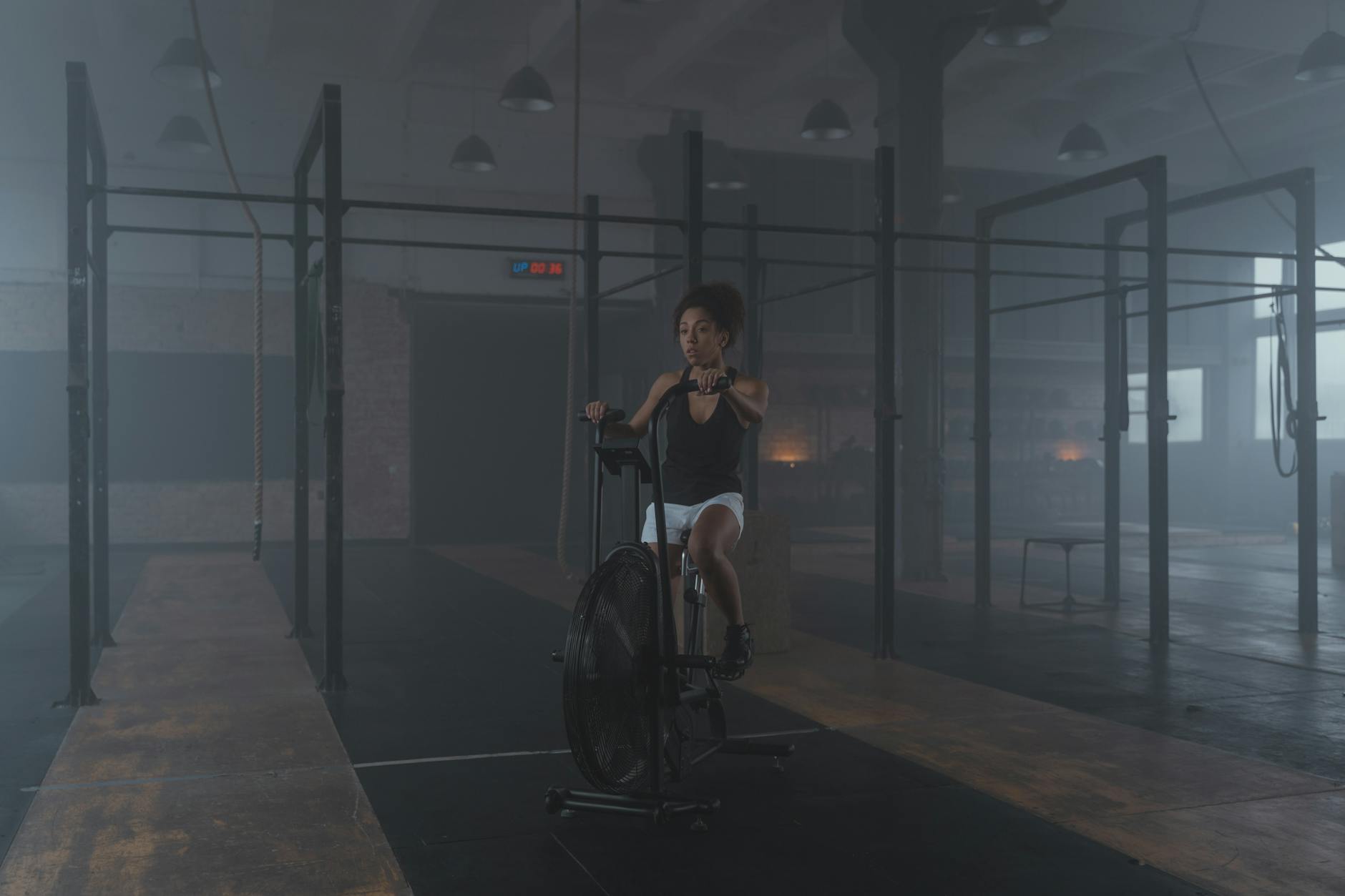 A woman works out on a stationary bike in a dimly lit gym setting, promoting fitness and healthy living. - crossfit workout plan