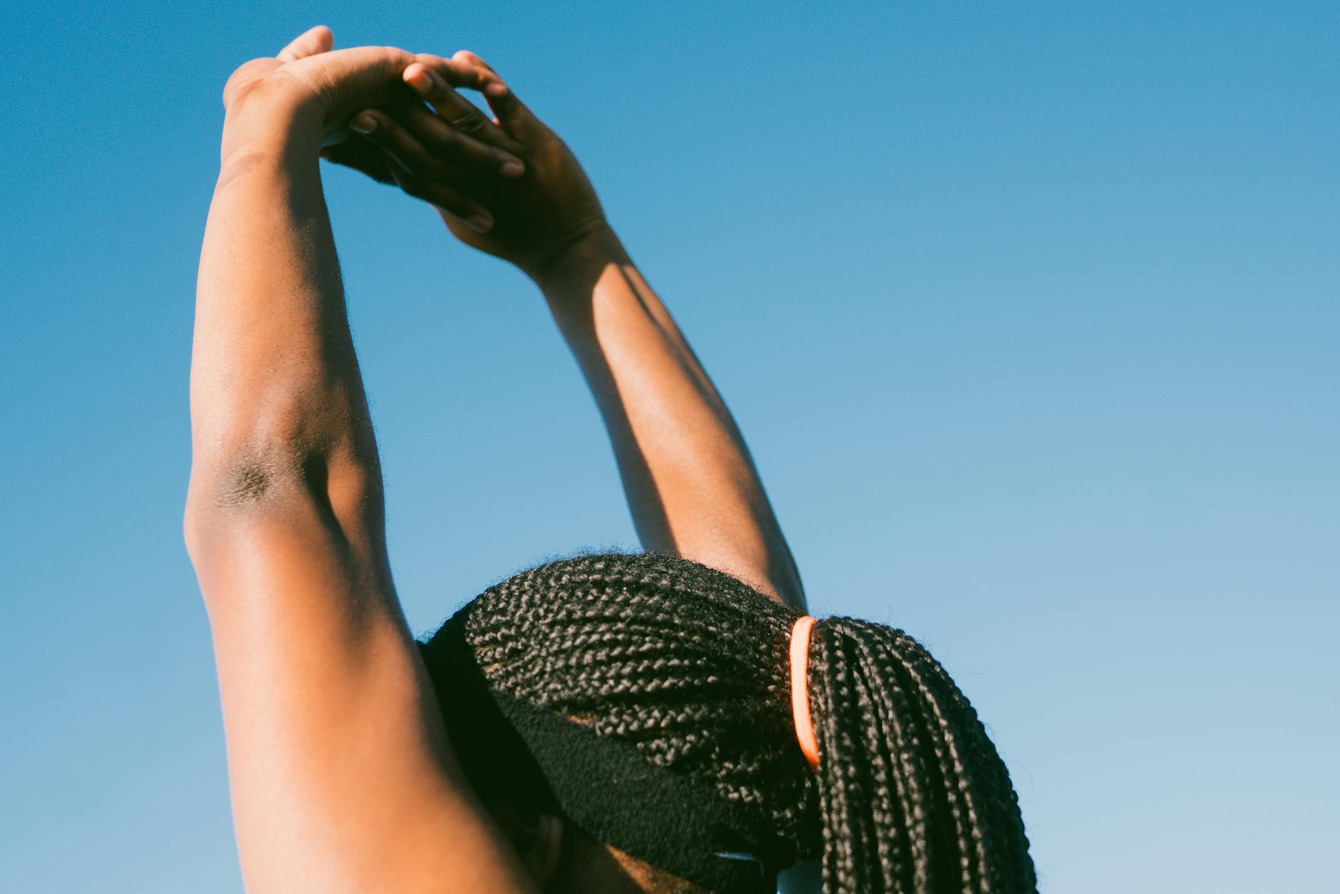 Person stretching outdoors with braided hair against a clear blue sky for a healthy lifestyle concept. - daily stretching routine