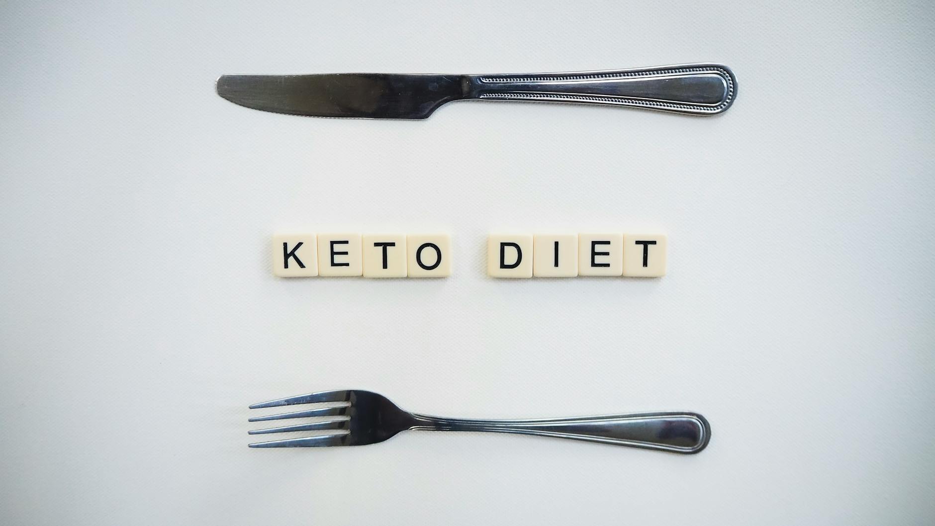 Top view of a knife, fork, and scrabble tiles spelling 'Keto Diet' on a white surface. - dash diet plan