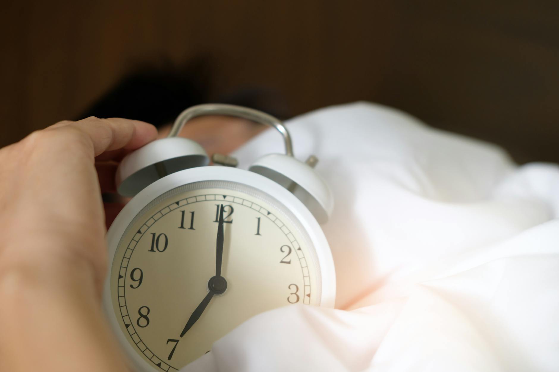 A close-up of a hand reaching for a ringing alarm clock, symbolizing waking up in the morning. - daylight sleep science