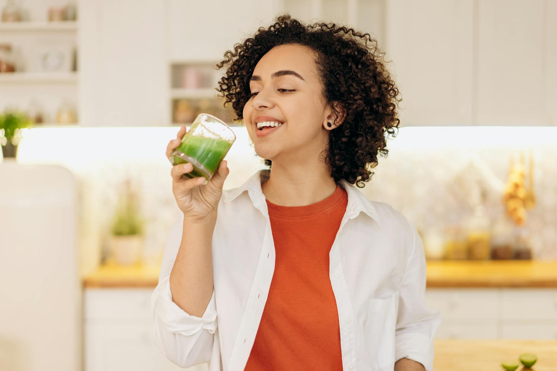 Smiling woman enjoys a fresh green smoothie in a cozy kitchen, promoting a healthy lifestyle. - how to detox