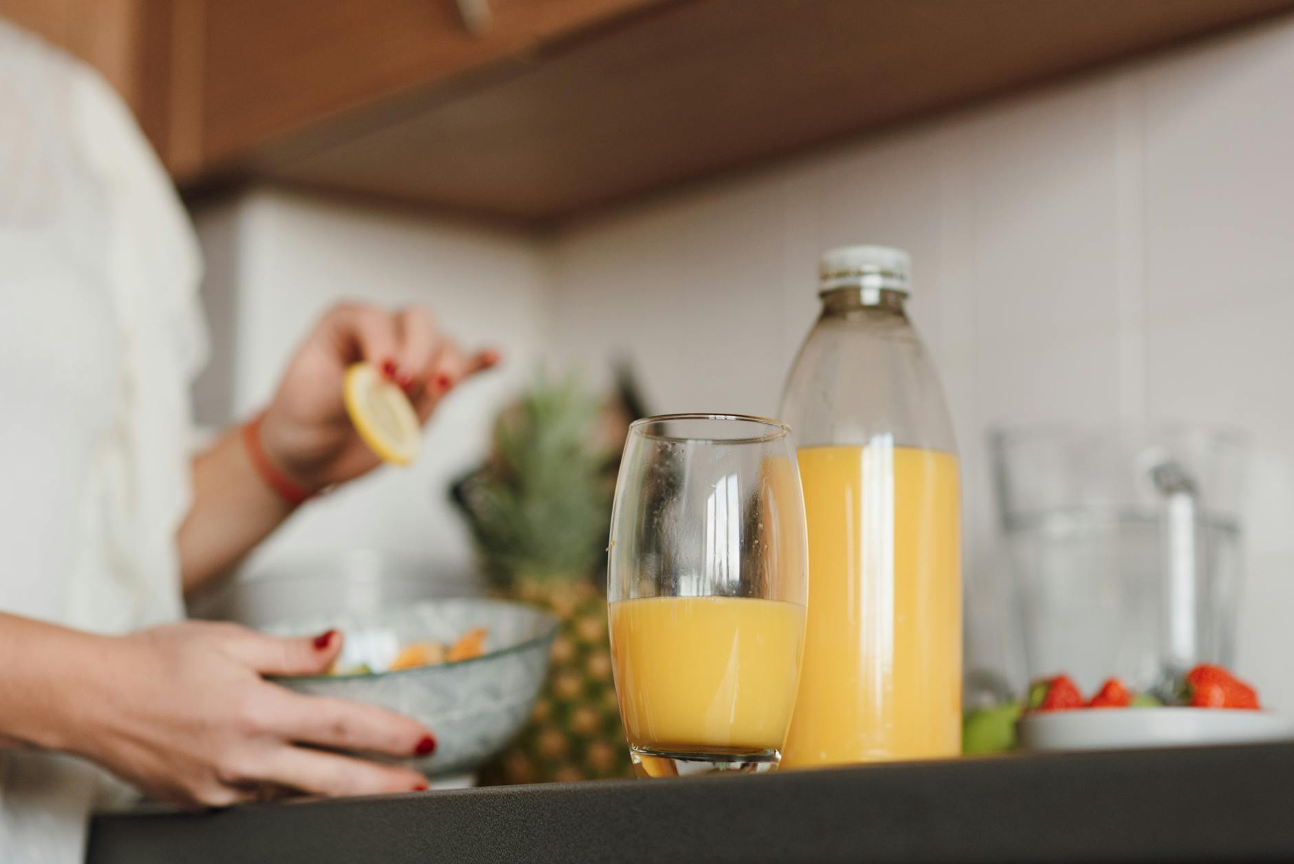 Woman preparing fresh citrus juice in a modern kitchen setting with fruits and glass bottle. - detox drink recipes