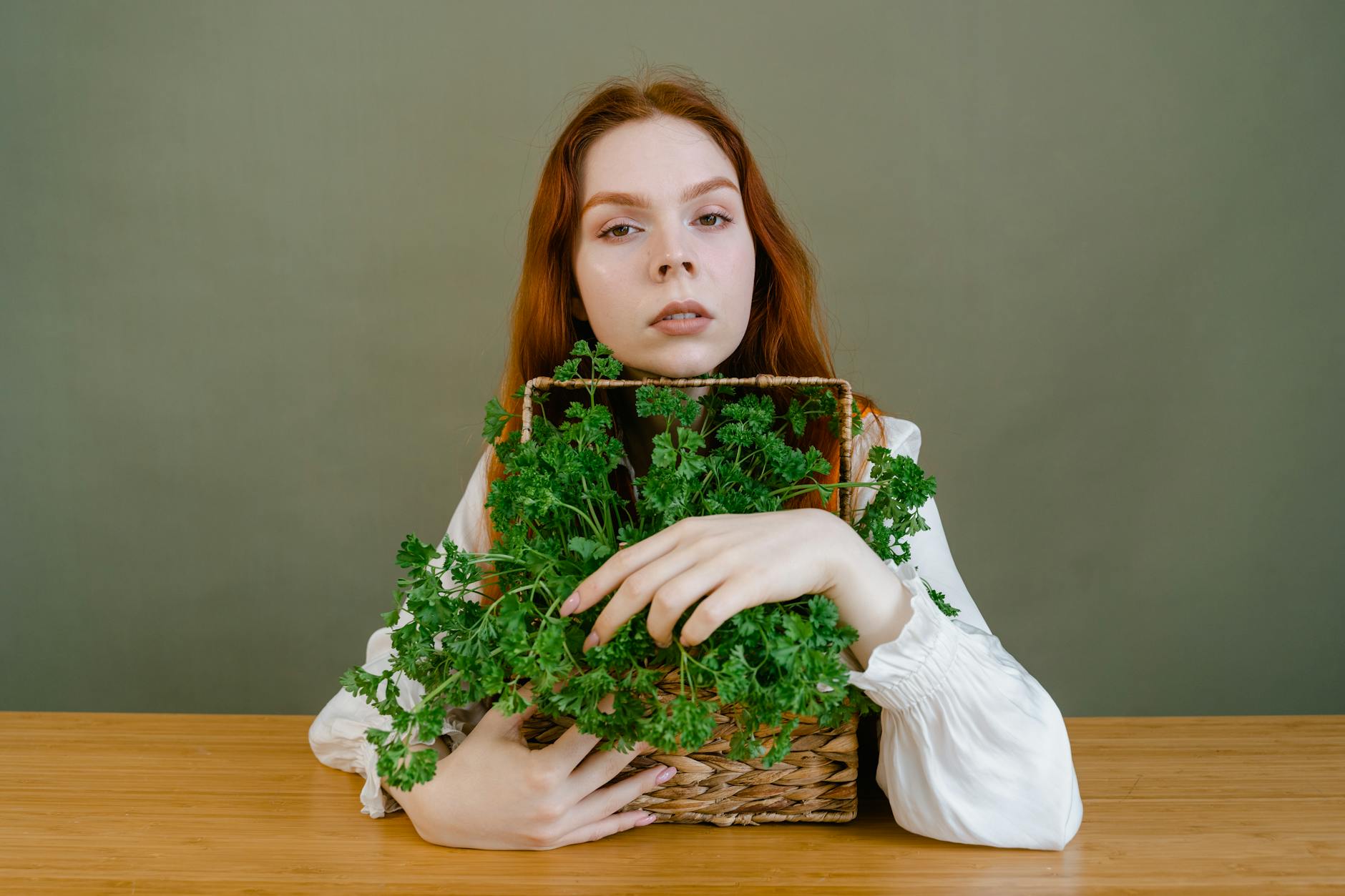 A young woman with ginger hair holds a basket of fresh parsley against a green background. - diet detox spring