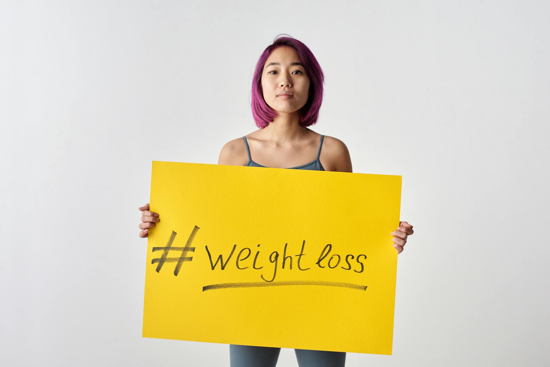 Asian woman with purple hair holding a weight loss sign in a studio setting. - easy weight loss