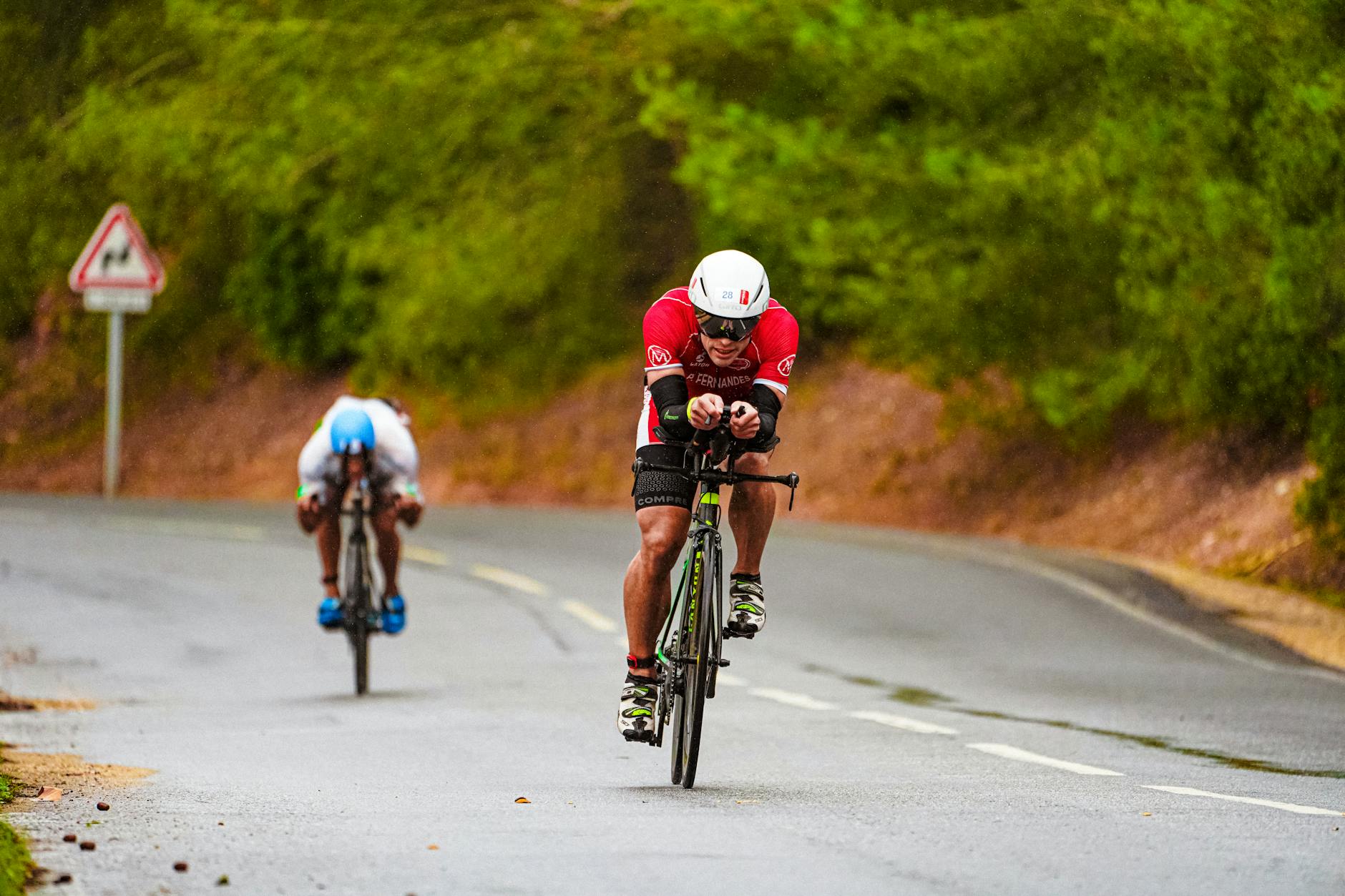 Full body of focused young slender bicyclists in sportswear and helmets holding handlebars while riding bikes on uneven road out of city - endurance cycling training