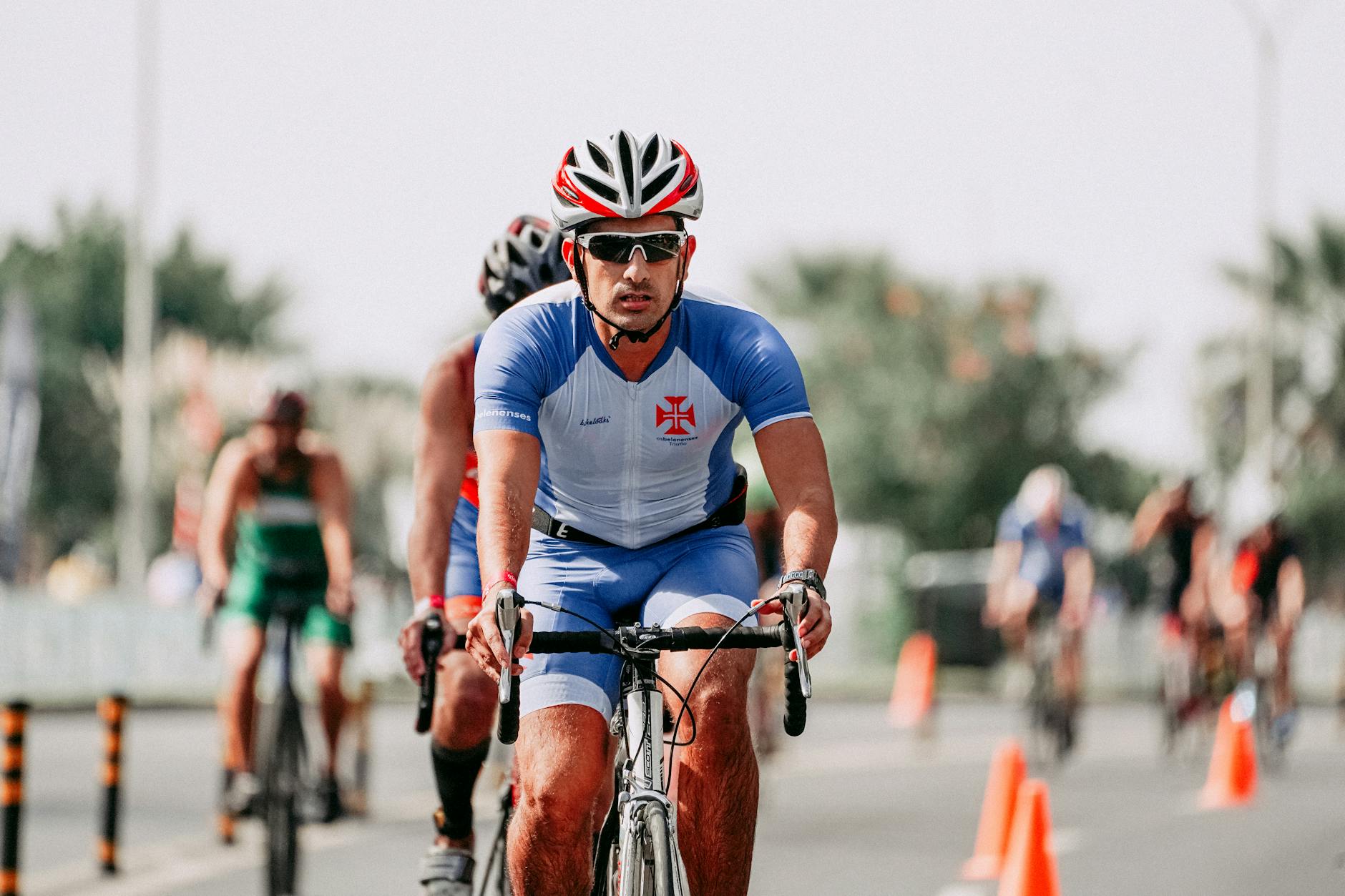 Serious male athlete in sportswear and helmet riding bicycle near anonymous competitors during race on roadway - endurance cycling training