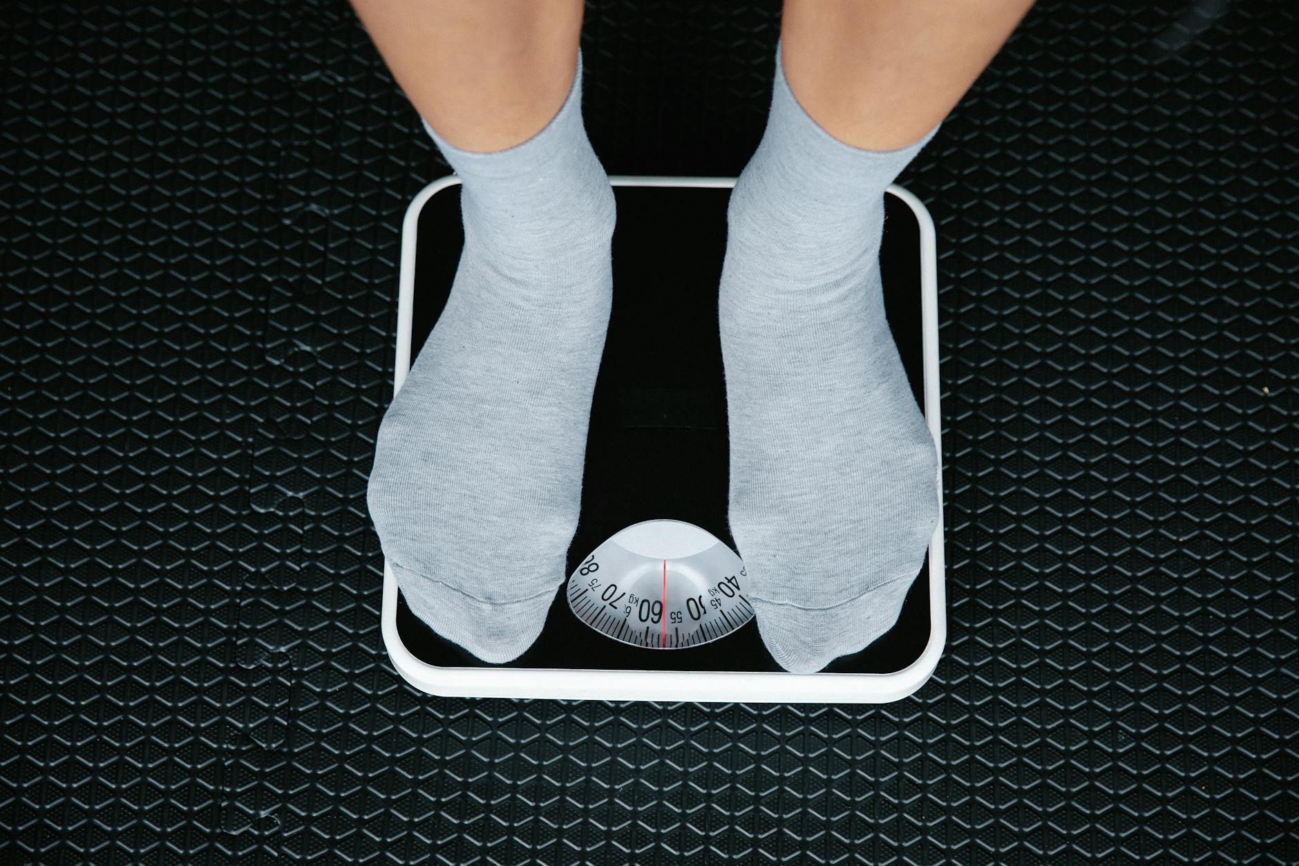Top view of feet in socks standing on a bathroom scale, indicating weight measurement. - fitness weight loss plan