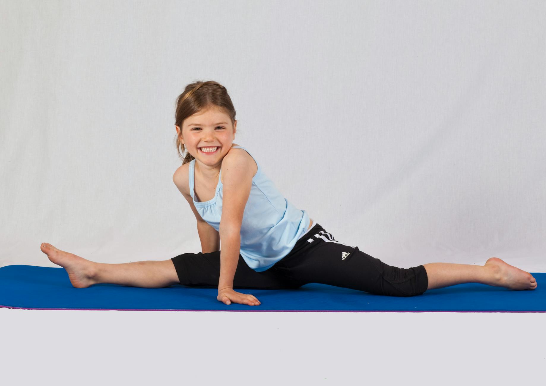 Smiling young girl performing a split on a yoga mat indoors, showcasing flexibility and joy in exercise. - flexibility exercises list