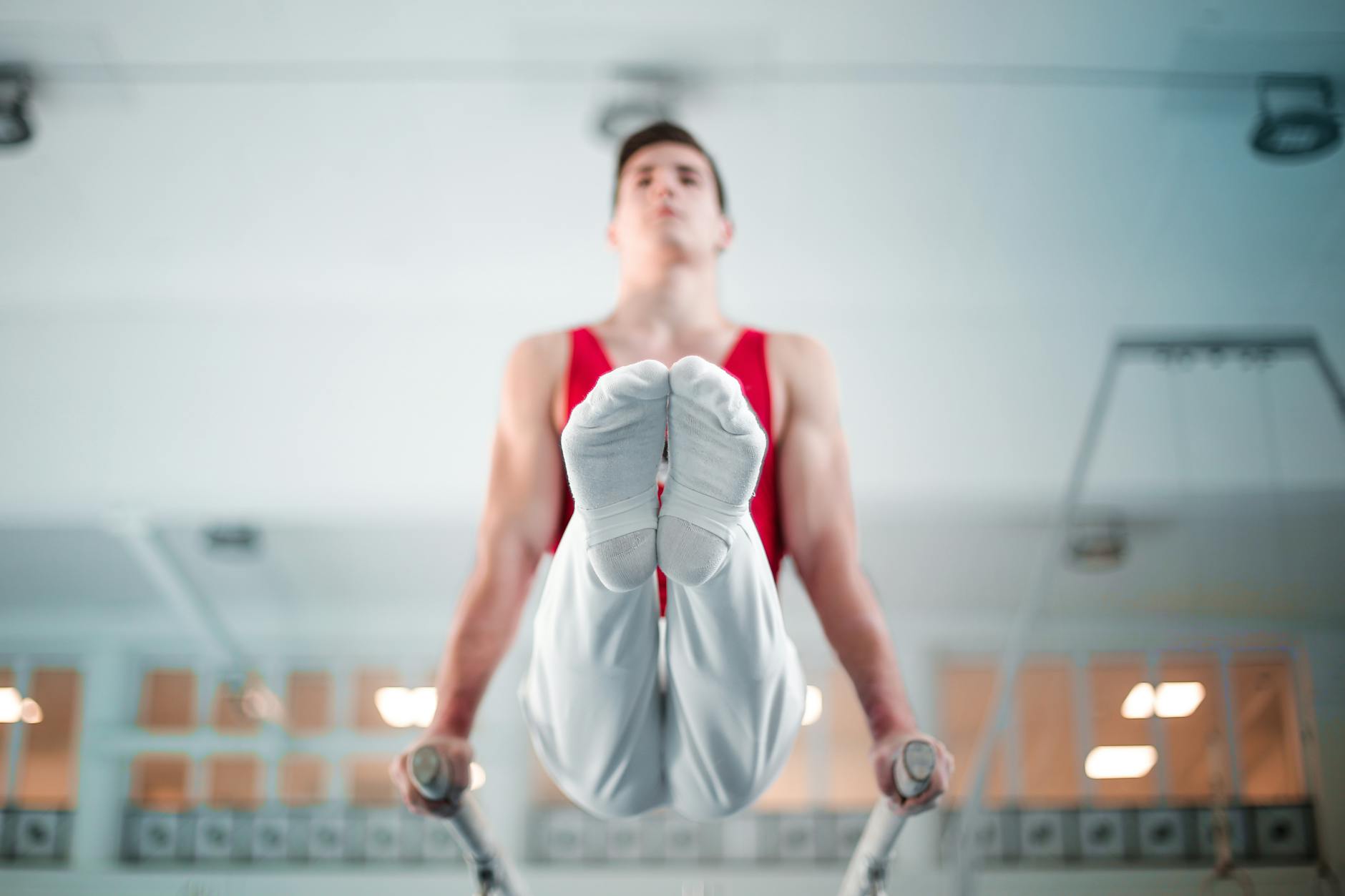 A male gymnast demonstrates strength and balance on parallel bars indoors. - hamstring flexibility exercises
