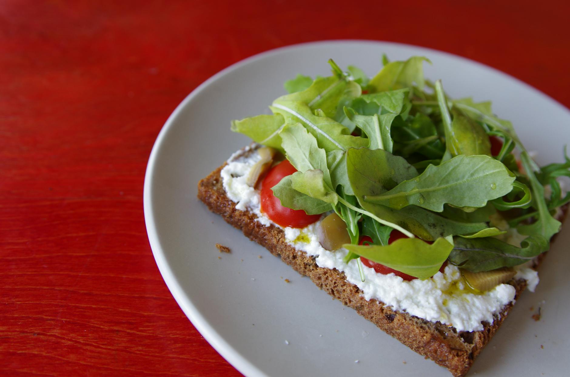 Tasty open-faced sandwich with arugula, cheese, and tomatoes on a plate. - healthy breakfast sandwich