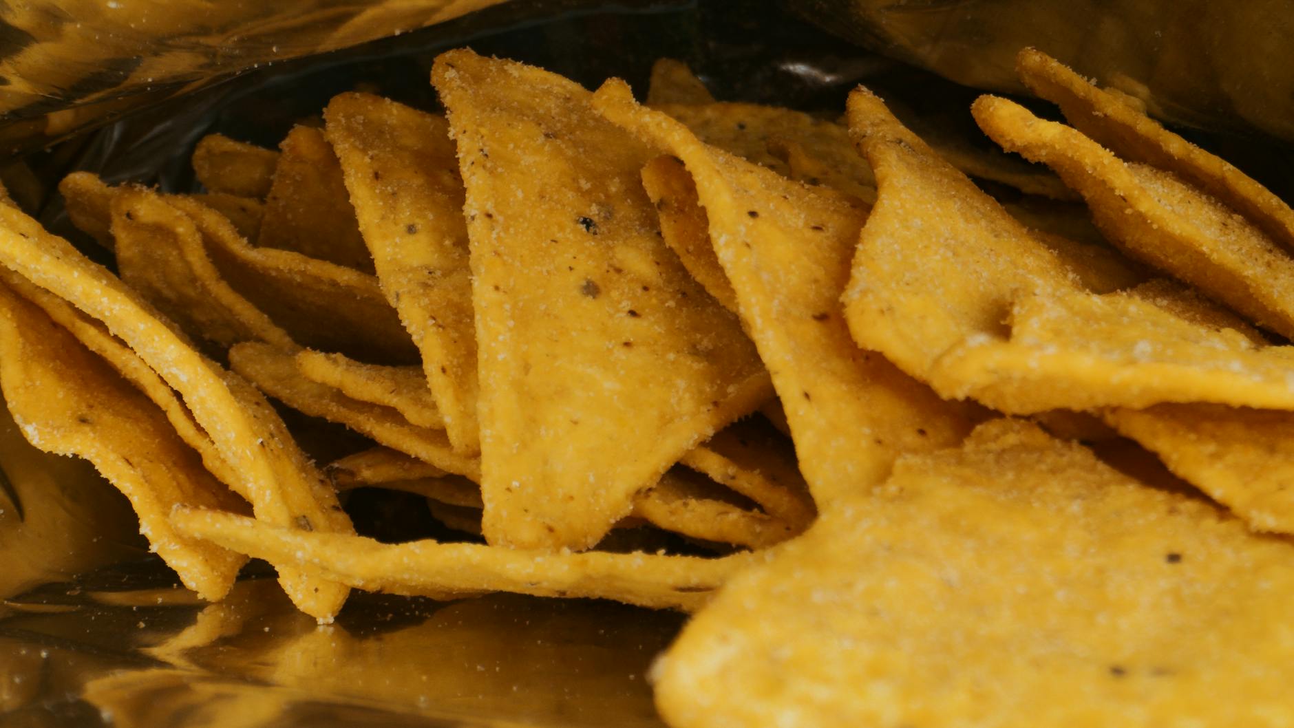 A detailed view of crispy nacho chips inside a metallic snack package. - healthy chips