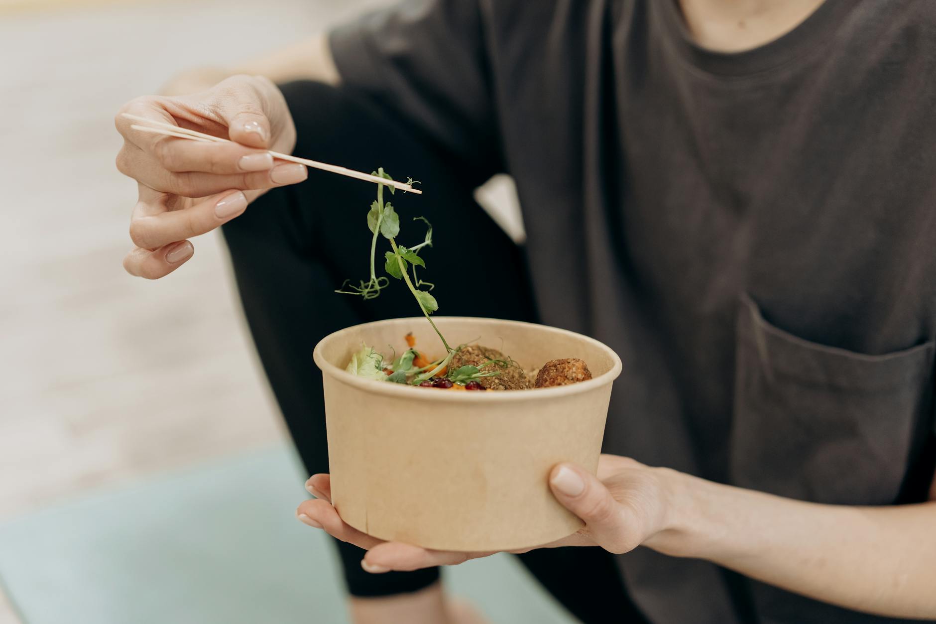 A woman holding a paper bowl filled with a healthy vegetarian meal in an indoor setting, promoting wellness. - healthy diet plan