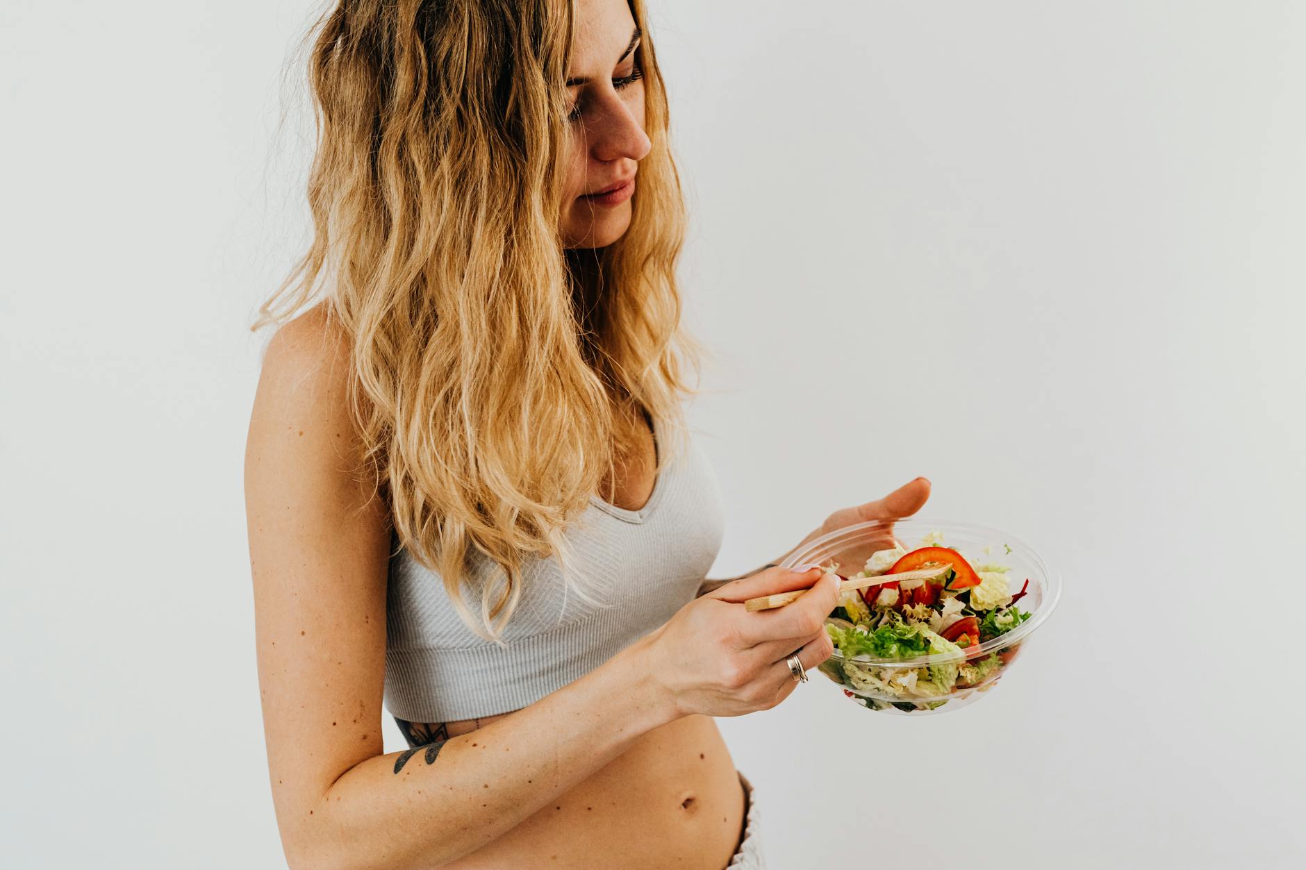 A caucasian woman in a sports bra enjoying a fresh salad, embodying healthy eating and lifestyle. - healthy diet swaps